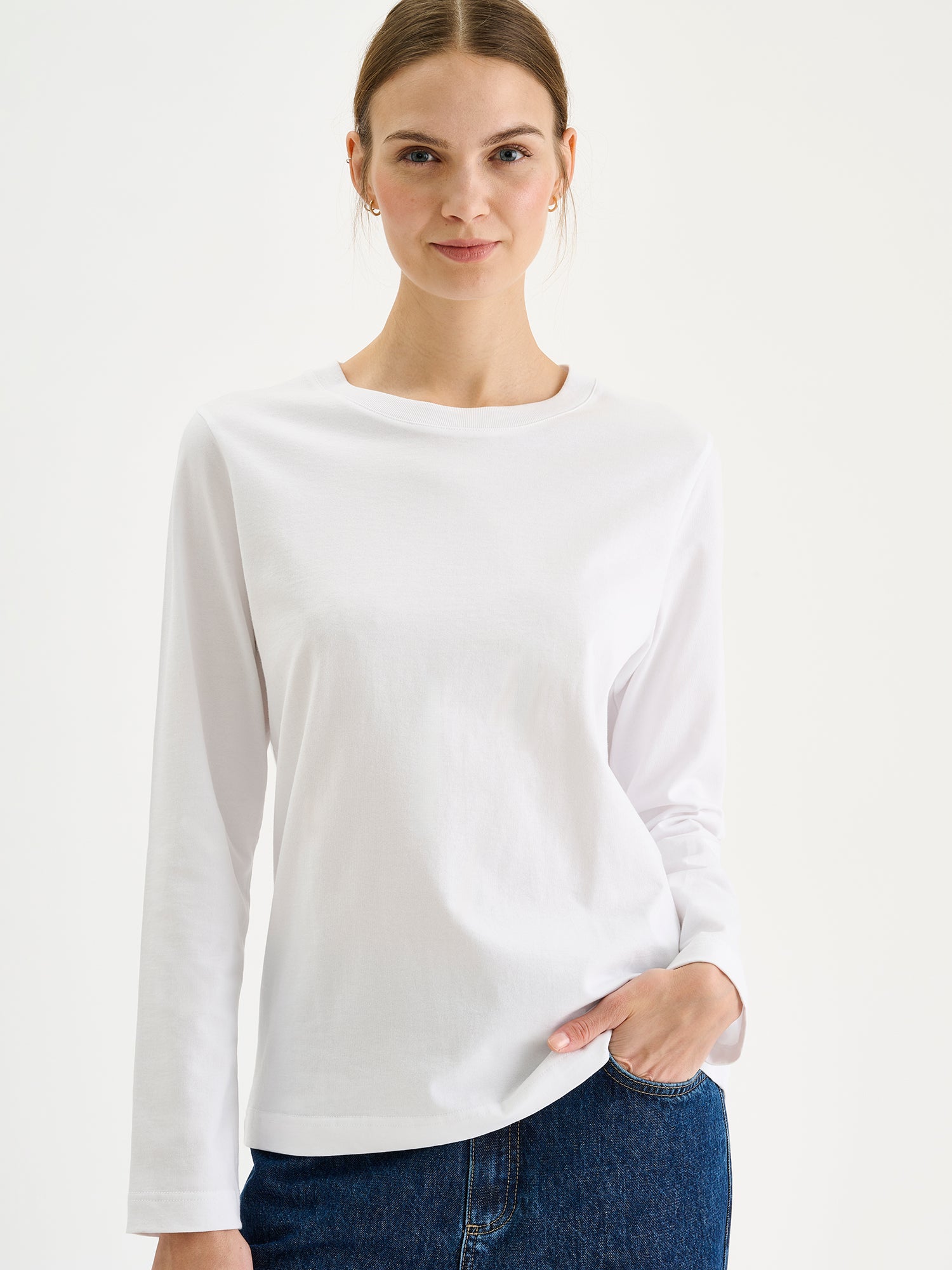 Nanso womens white NORMI Long-Sleeved T-Shirt is a versatile piece that features a classic crew neckline and full-length sleeves for everyday versatility. Pictured on a model with blue jeans, close-up.