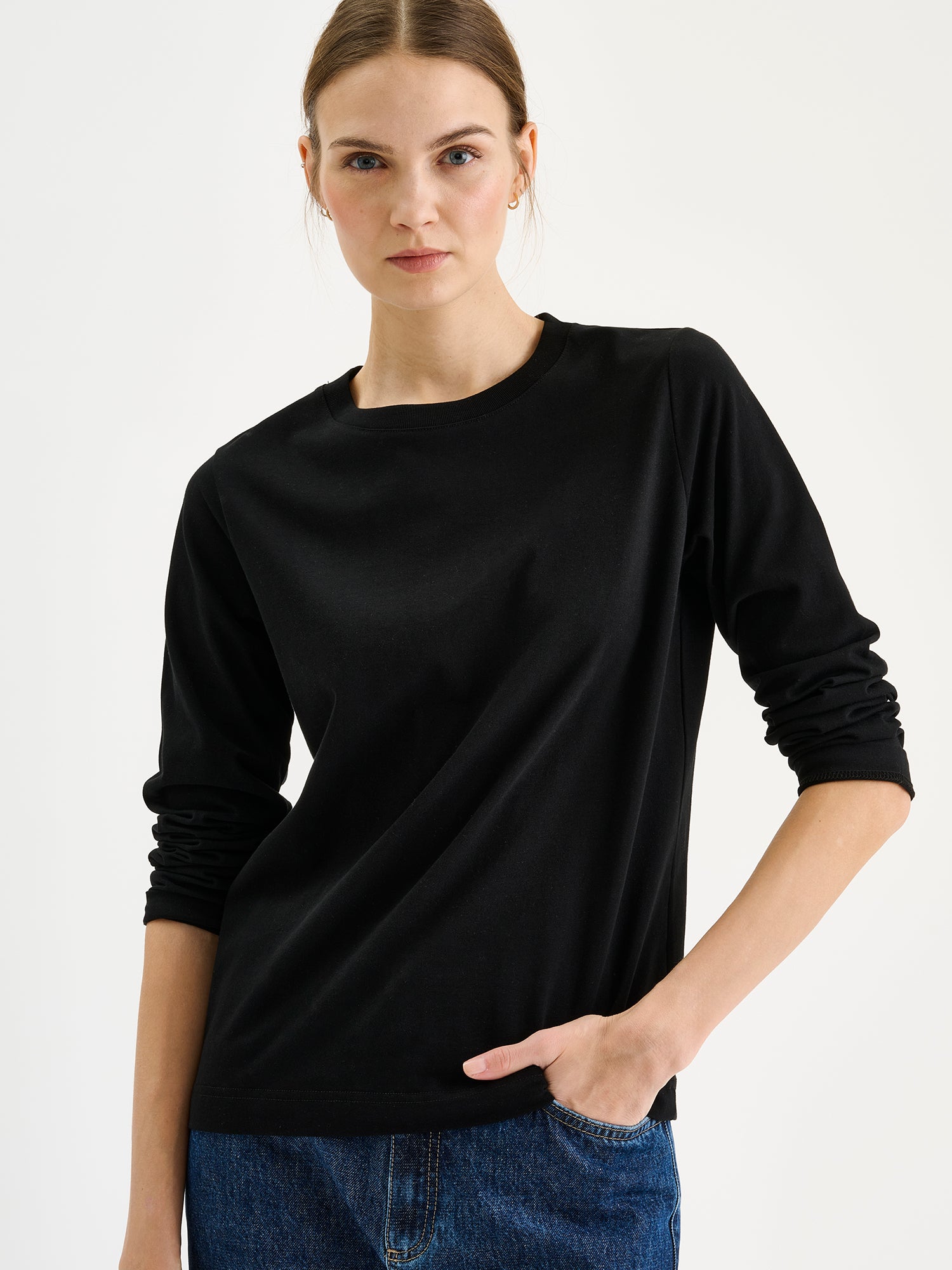 Nanso womens black NORMI Long-Sleeved T-Shirt is a versatile piece that features a classic crew neckline and full-length sleeves for everyday versatility. On a model with blue jeans, close-up.