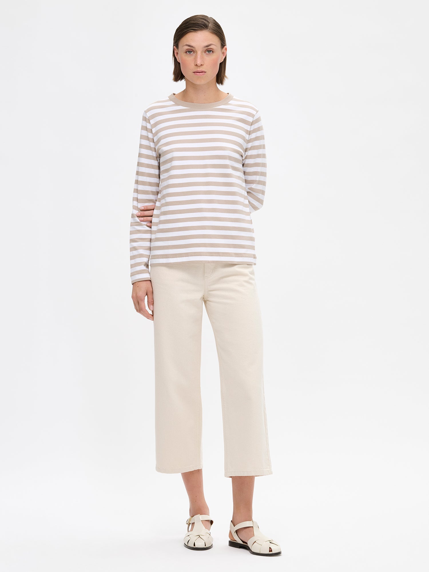 The RAITA NORMI Long-Sleeved Shirt in beige featuring striped pattern. The straight-cut shirt features a round neckline and full-length sleeves. 100% organic cotton. Pictured on a model with jeans.