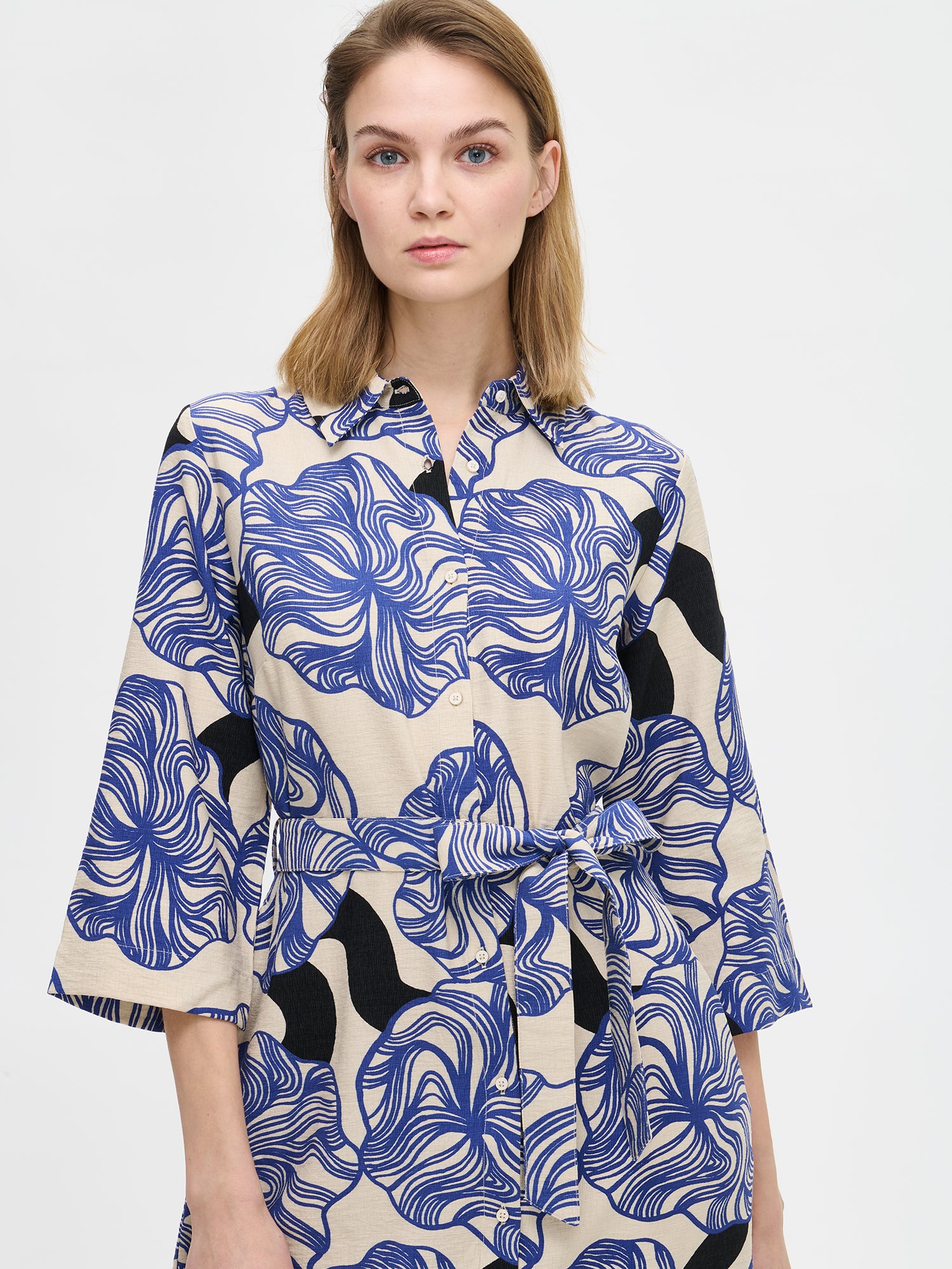 Nanso KOSMO Dress combines timeless elegance with a striking blue pattern, adjustable waist belt for a customized fit and practical pockets. On a model, close-up.
