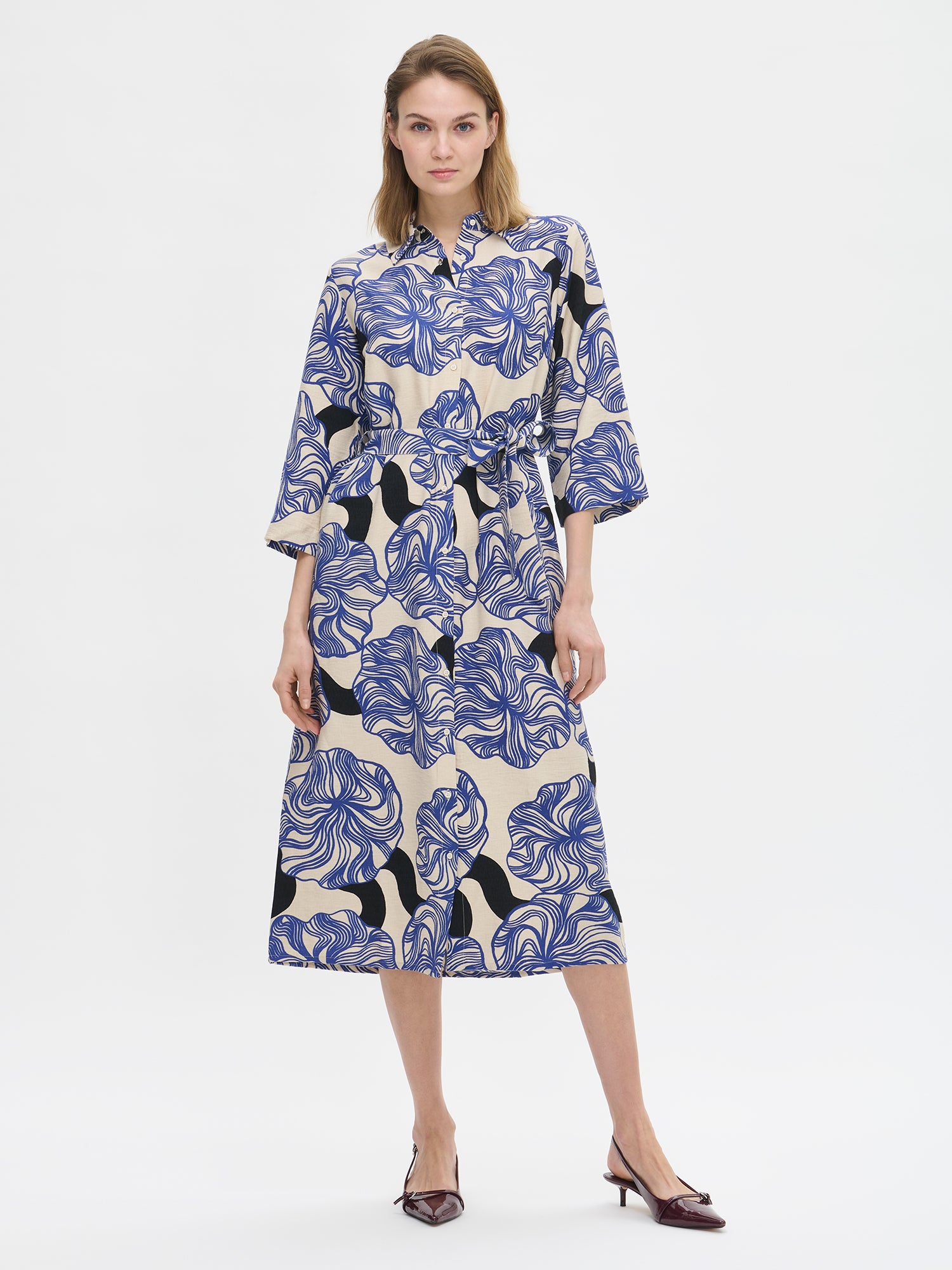 Nanso KOSMO Dress combines timeless elegance with a striking blue pattern, adjustable waist belt for a customized fit and practical pockets. On a model with high heels.