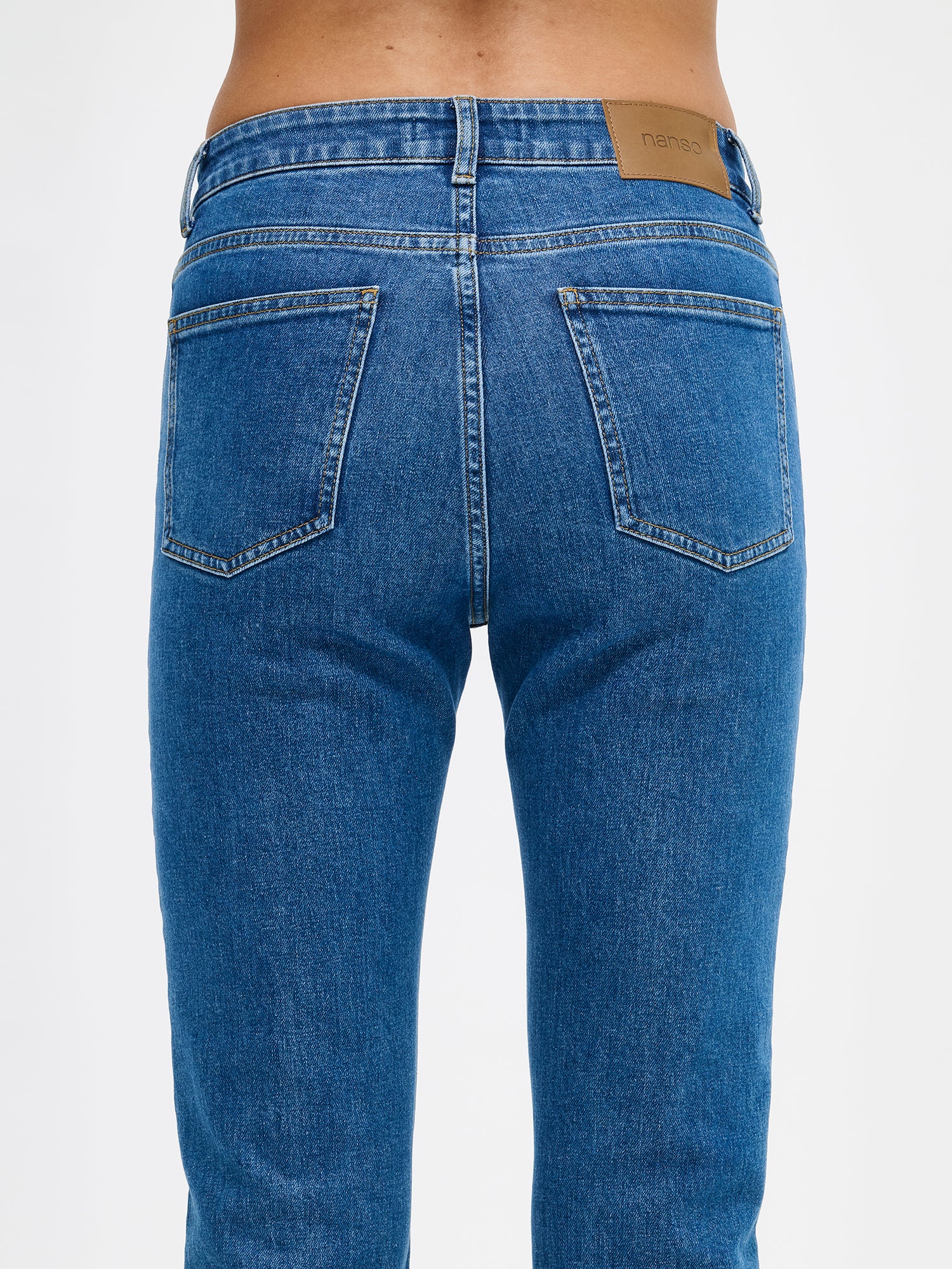 Nanso Cropped Kapee jeans feature a classic mid-rise waistband with a zippered fly and button closure for a secure fit. Practical front and back pockets provide convenient storage. On a model from the back, close-up.