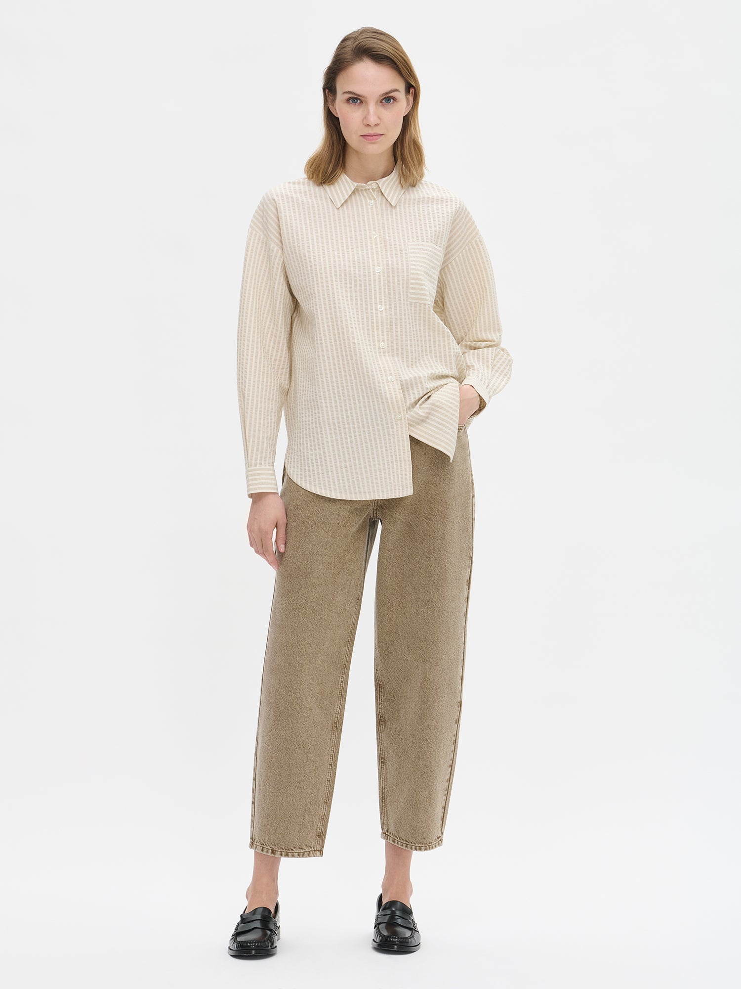 Nanso women's relaxed barrel leg Rento jeans in brown with an effortlessly comfortable fit.
Classic five-pocket design with a mid-rise waistband, front zip and button closure. On a model with a striped shirt.