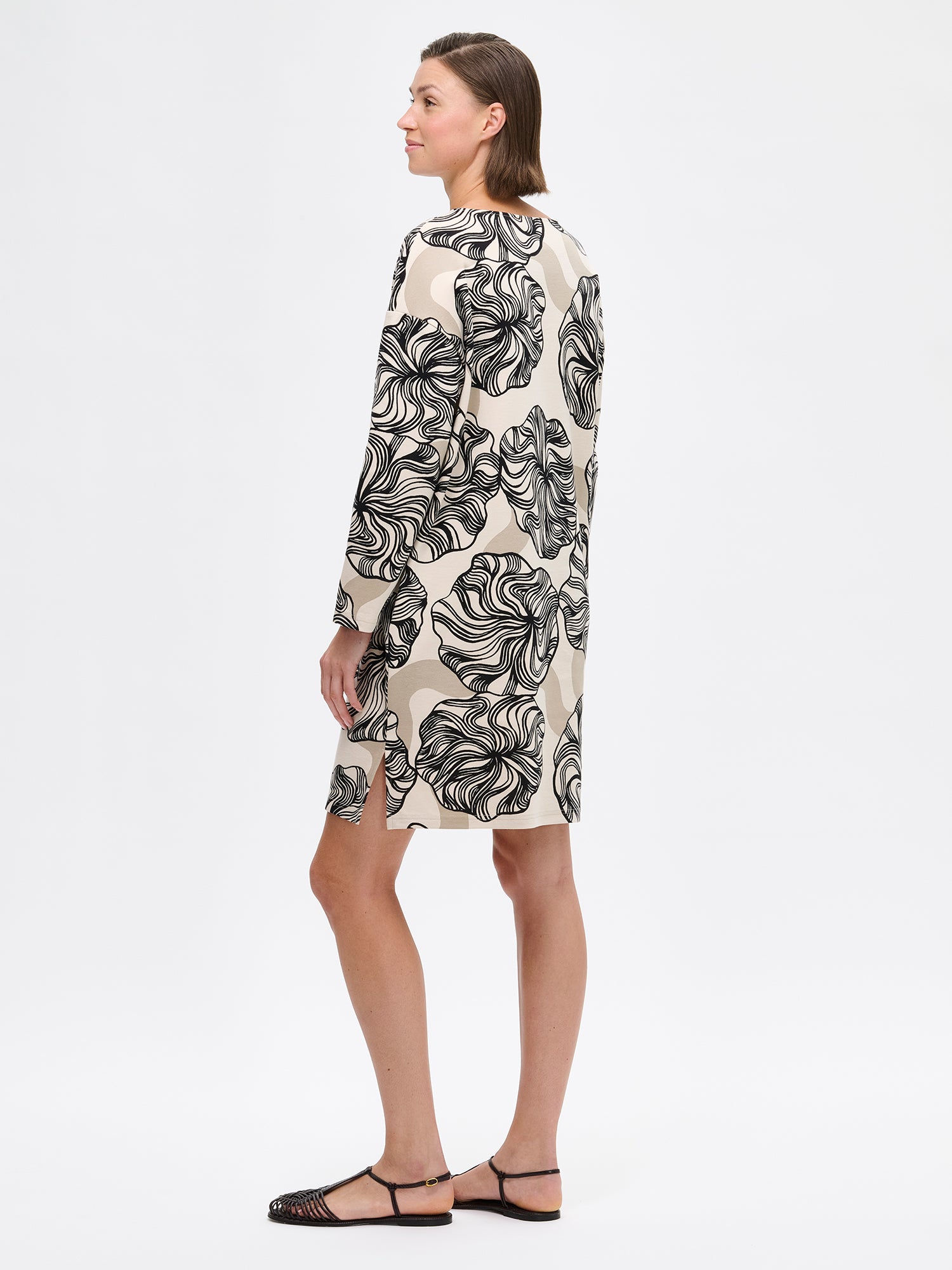 Nanso KOSMO Dress with graphic pattern on a minimalist silhouette features practical pockets, a classic boat neckline paired with dropped shoulders and full-length sleeves. On a model photographed from the side.