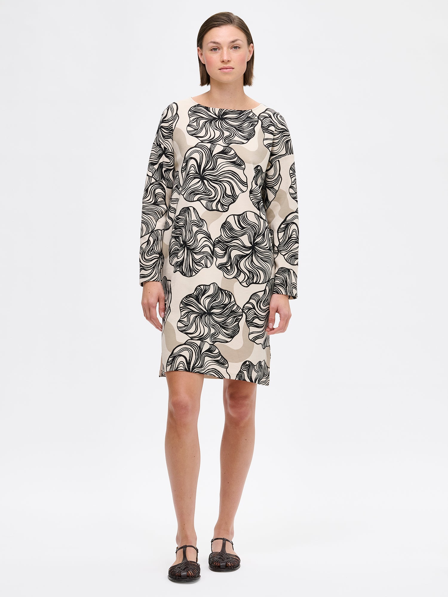 Nanso KOSMO Dress with graphic pattern on a minimalist silhouette features practical pockets, a classic boat neckline paired with dropped shoulders and full-length sleeves. on a model with sandals.