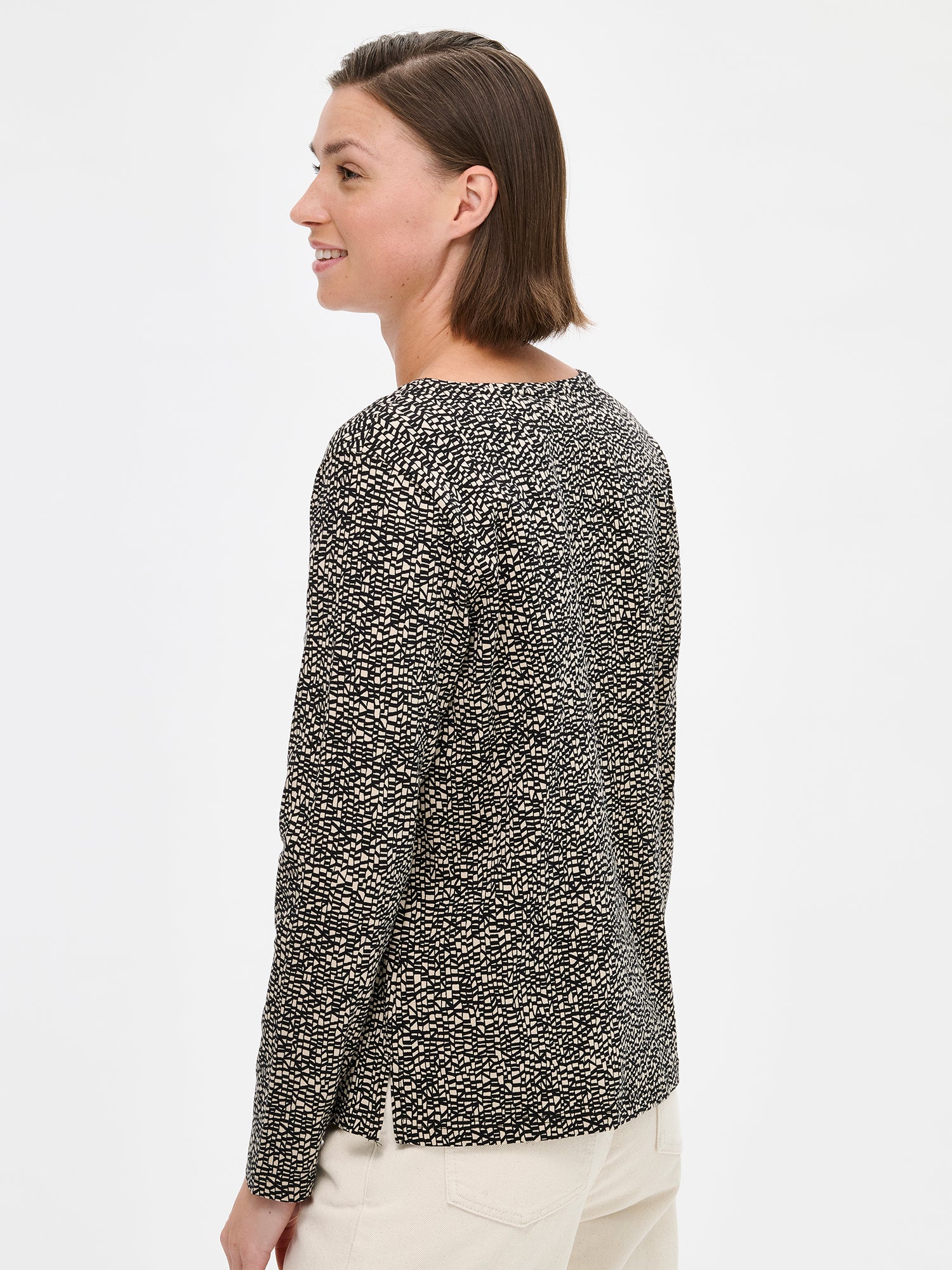 Nanso women's patterned Kaislat blouse in beige with a round neckline and full-length sleeves. On a model with wide off white jeans, pictured from the side.