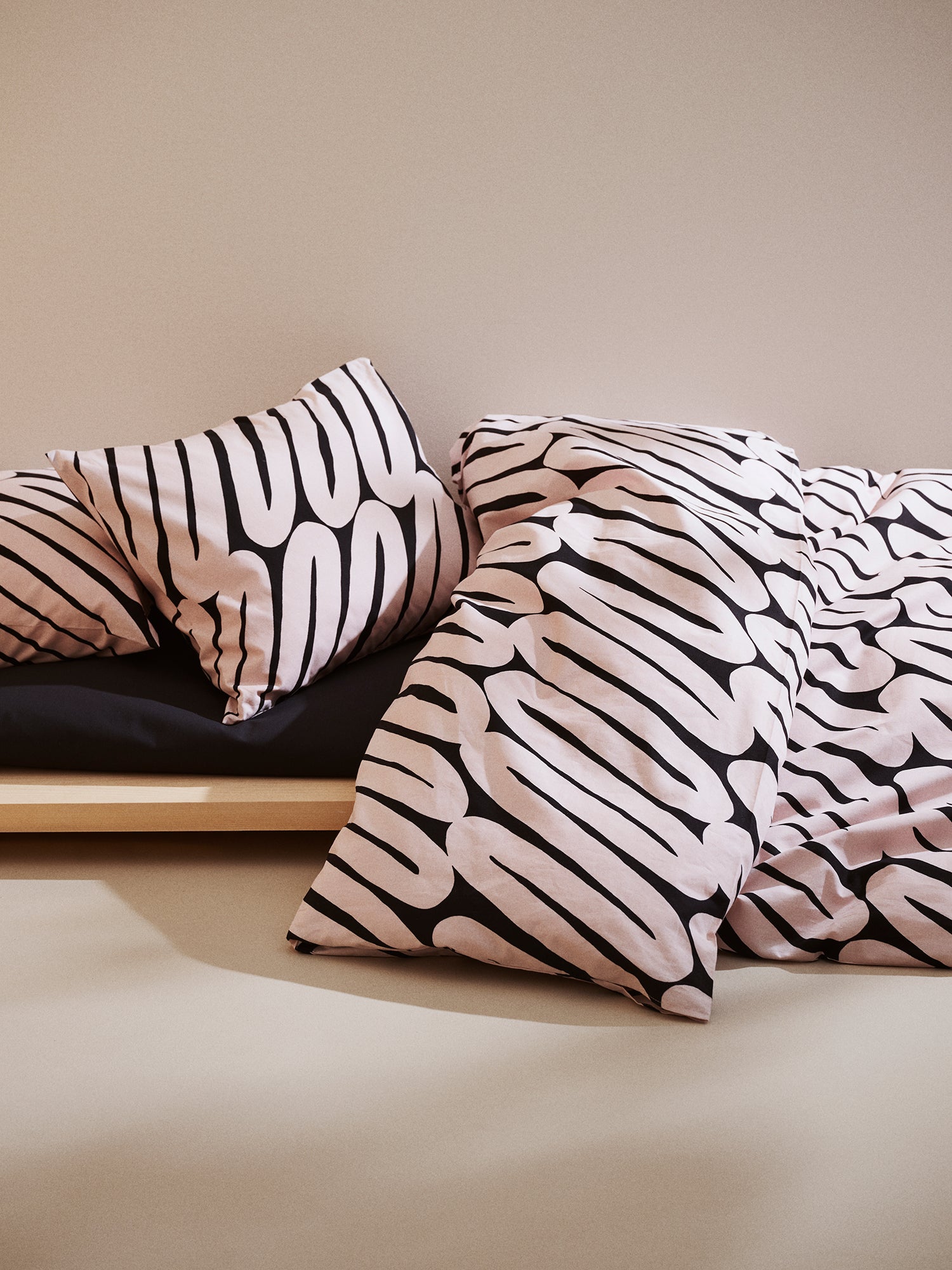 Laskos duvet cover set in bed setting combined with a black sheet in a beige room.