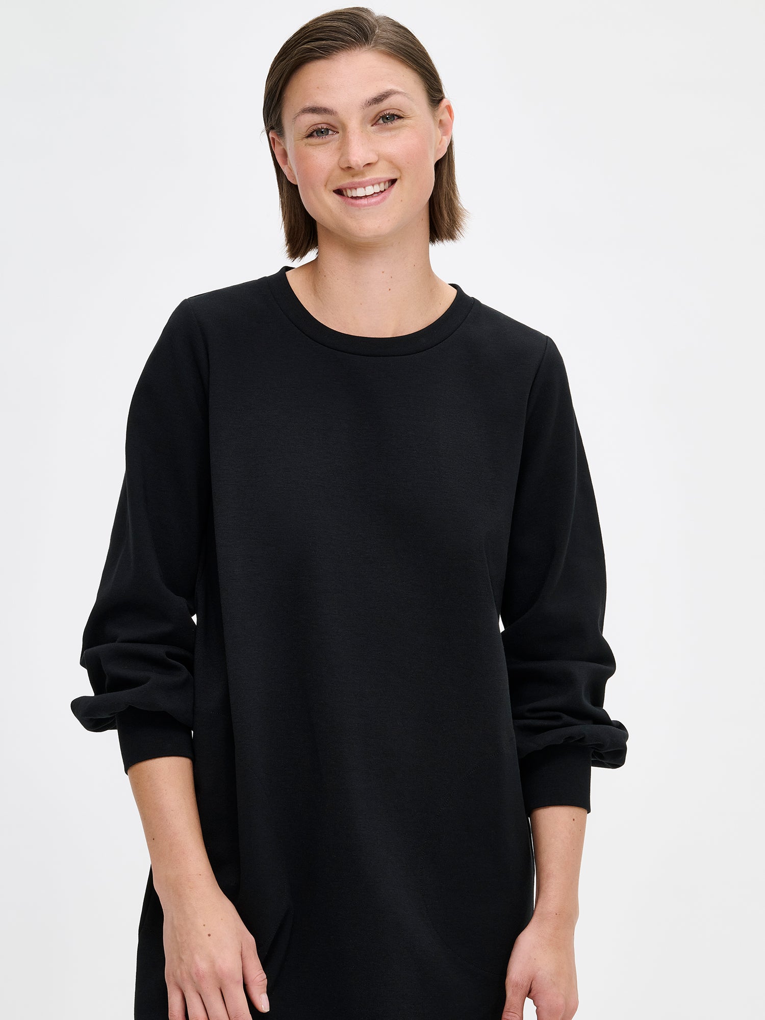 Nanso women's black Leija-dress. This straight-cut dress features a round neckline, side pockets, and full-length sleeves that gather beautifully at the cuffs. On a model, close-up.