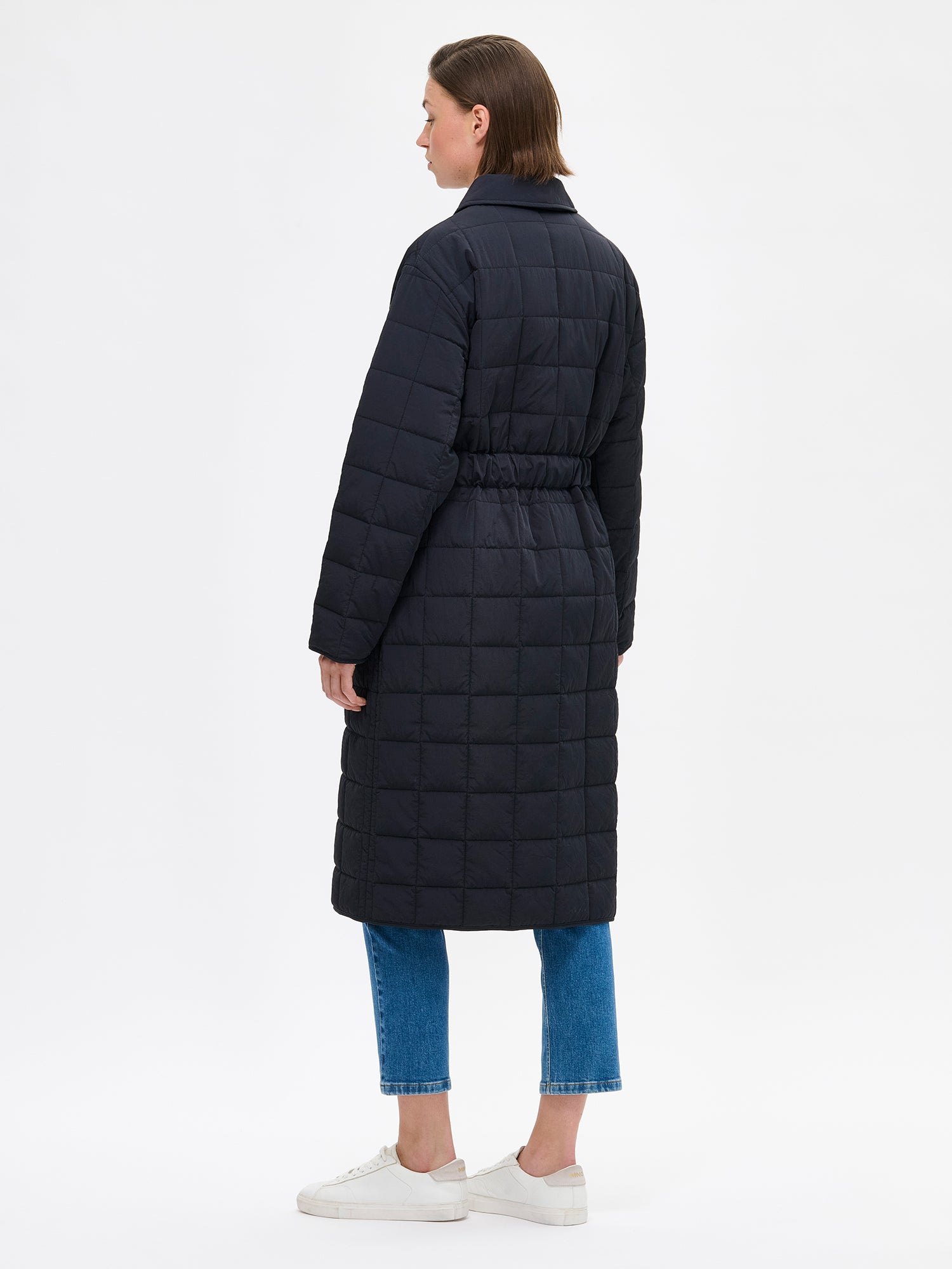 Nanso Marje Quilted Coat features classic collar styling and convenient snap closures at the front, a belt for a personalized fit, and practical front patch pockets. On a model photographed from the back.