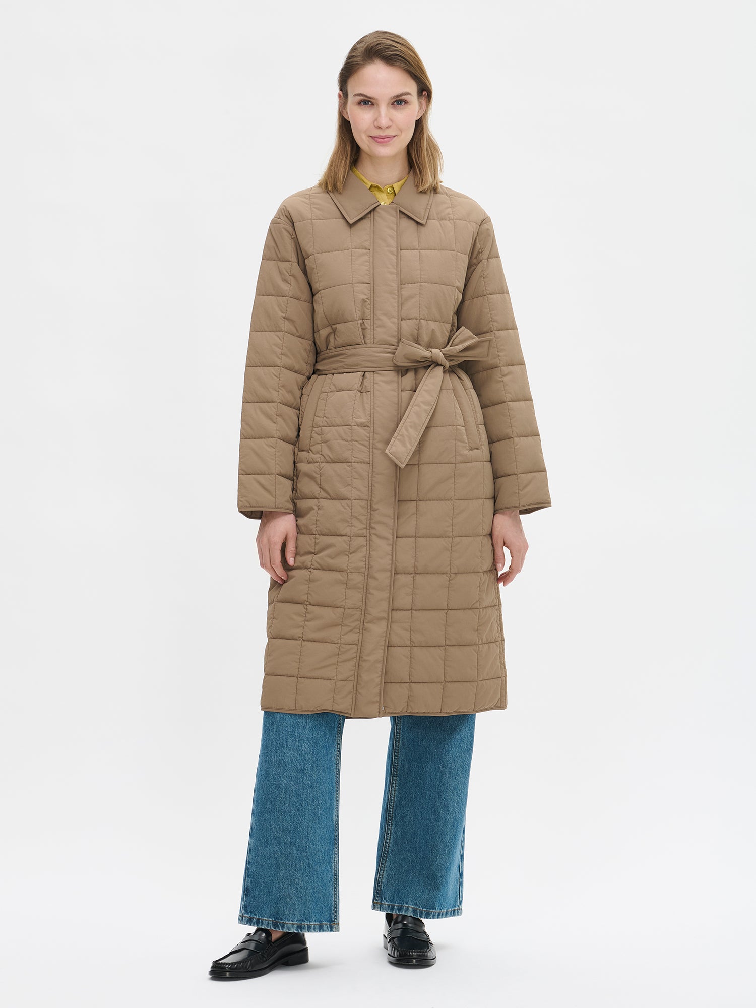 Nanso Marje Quilted Coat features classic collar styling and convenient snap closures at the front, a belt for a personalized fit, and practical front patch pockets. On a model with jeans, the coat closed.