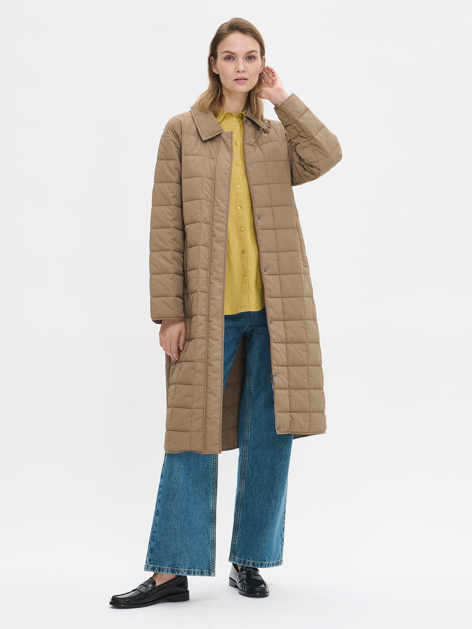 Nanso Marje Quilted Coat features classic collar styling and convenient snap closures at the front, a belt for a personalized fit, and practical front patch pockets. On a model with the coat open.