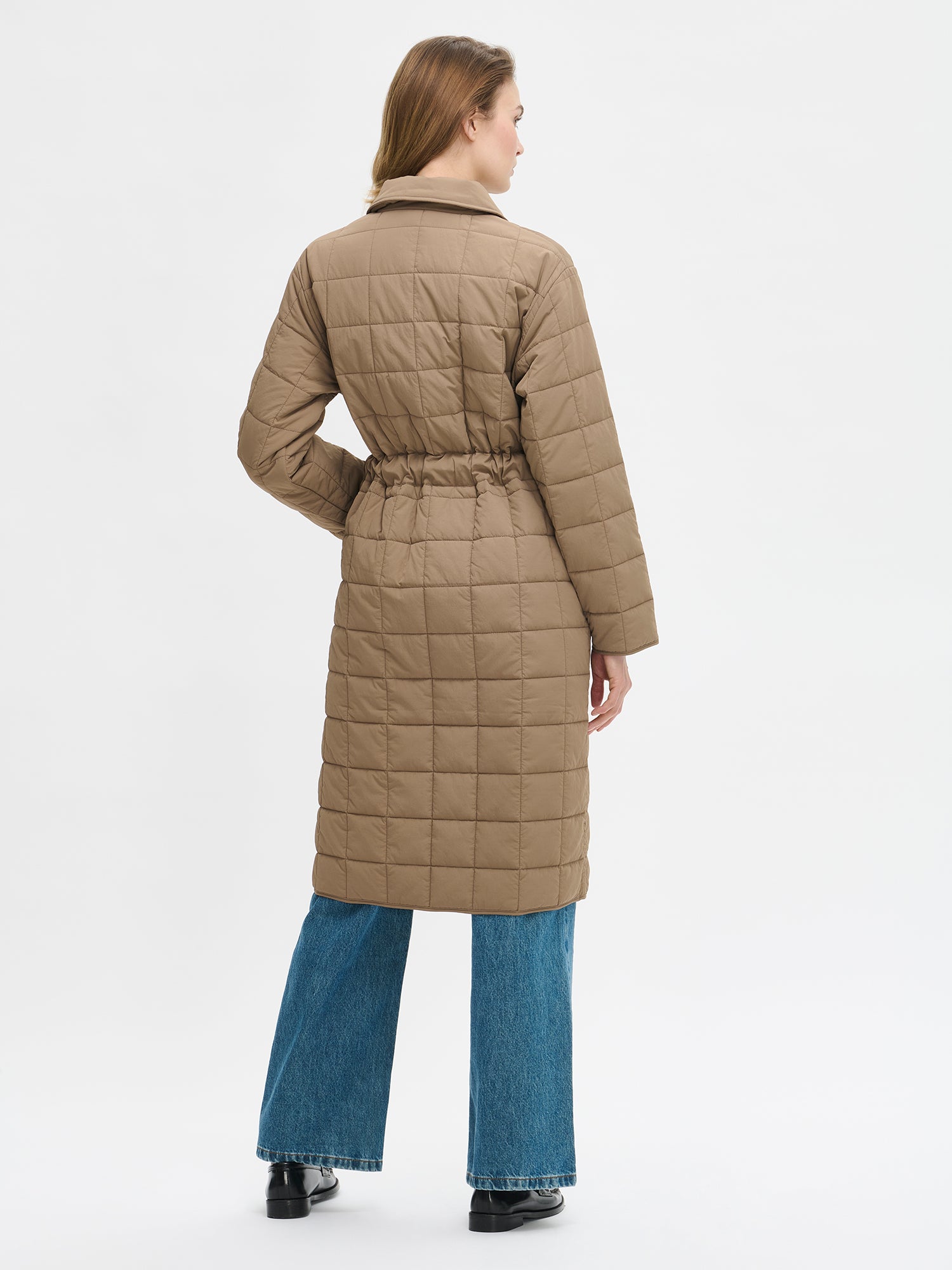 Nanso Marje Quilted Coat features classic collar styling and convenient snap closures at the front, a belt for a personalized fit, and practical front patch pockets. Photographed on a model from the back side.