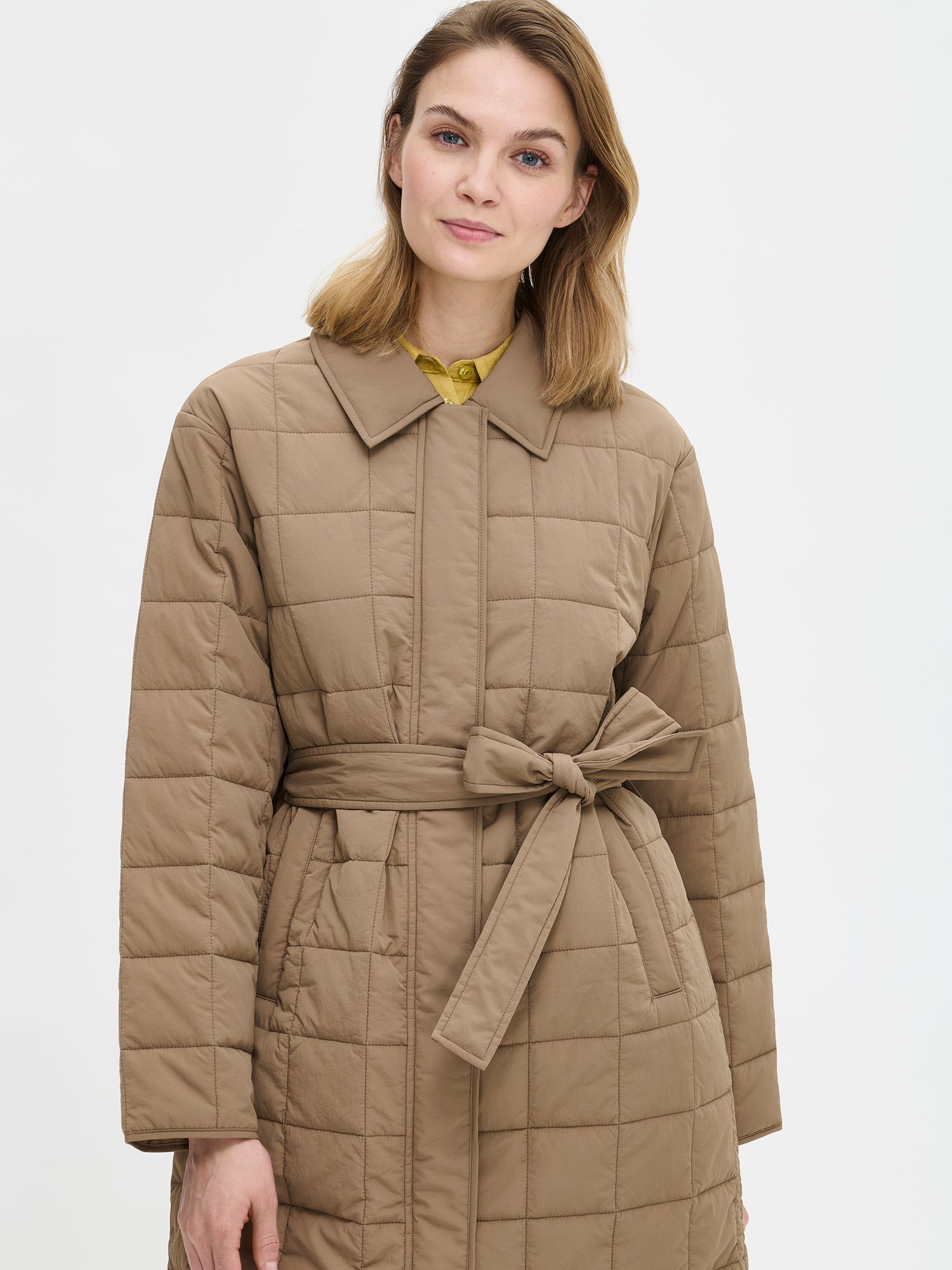 Nanso Marje Quilted Coat features classic collar styling and convenient snap closures at the front, a belt for a personalized fit, and practical front patch pockets. Pictured on a model, close-up.