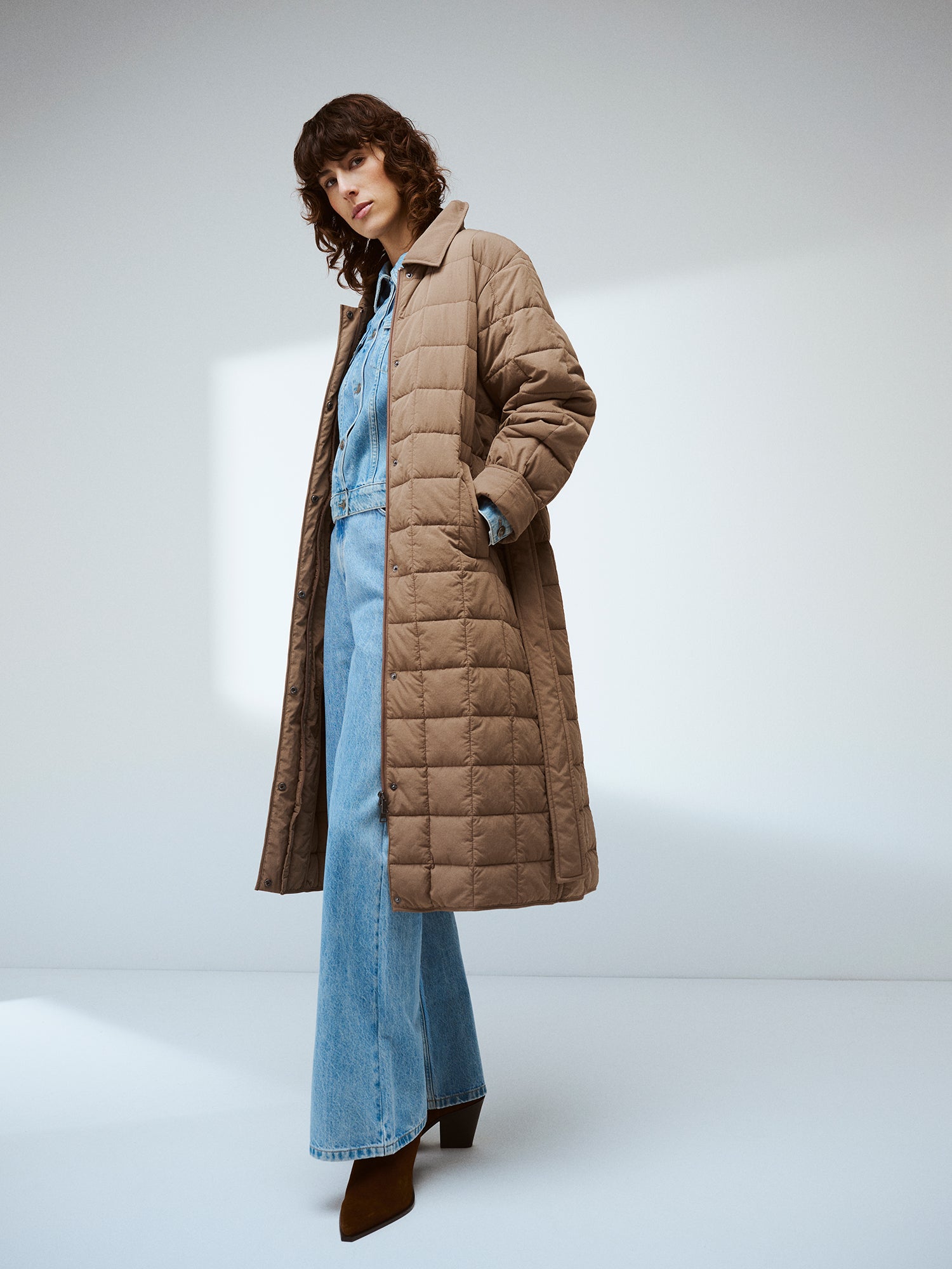 Nanso Marje Quilted Coat features classic collar styling and convenient snap closures at the front, a belt for a personalized fit, and practical front patch pockets. On a model in a brand picture.
