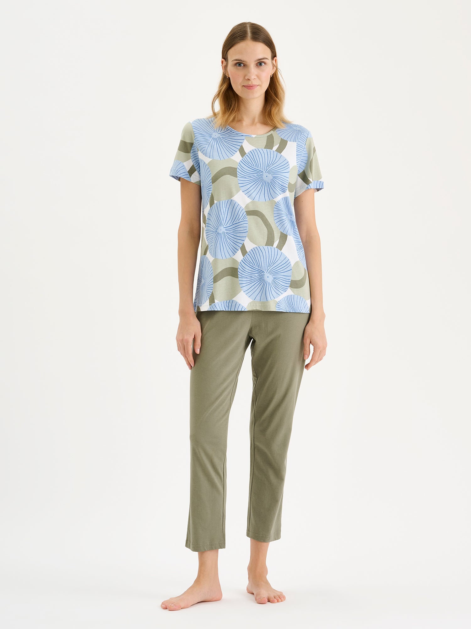 Soft and stylish, the HEDDA Pajamas feature a delicate blue-toned print on the short-sleeved top paired with olive-green bottoms. Pictured on a model.