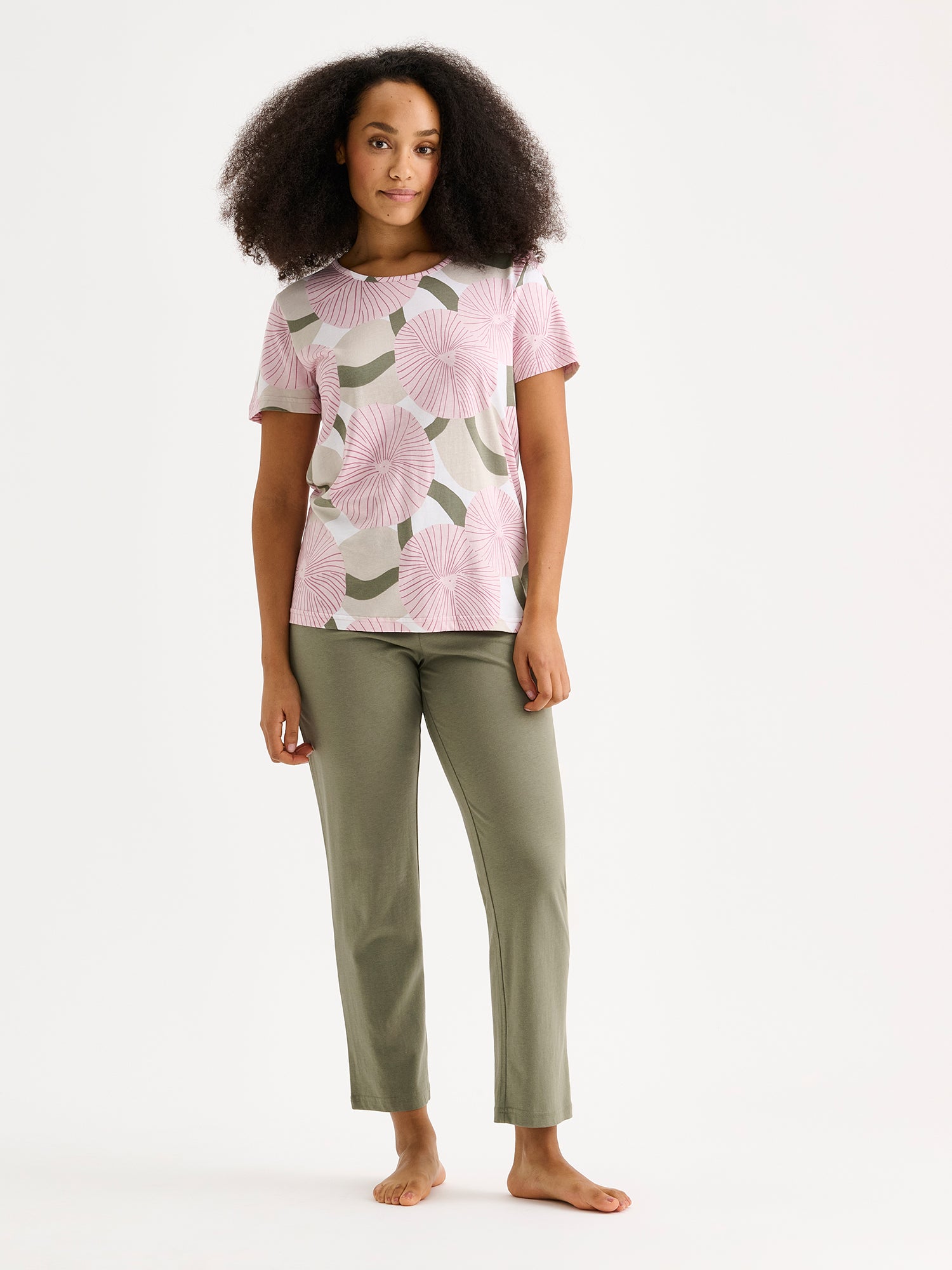 Soft and stylish, the HEDDA Pajamas feature a delicate pink-toned print on the short-sleeved top paired with olive-green bottoms. Pictured on a model.