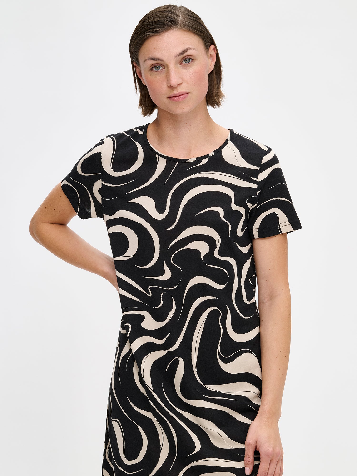 Nanso VESI short nightgown in black and beige tones with an elegant patterned design. Features a classic round neckline and relaxed fit and soft material for restful nights. On a model from the front, close-up.