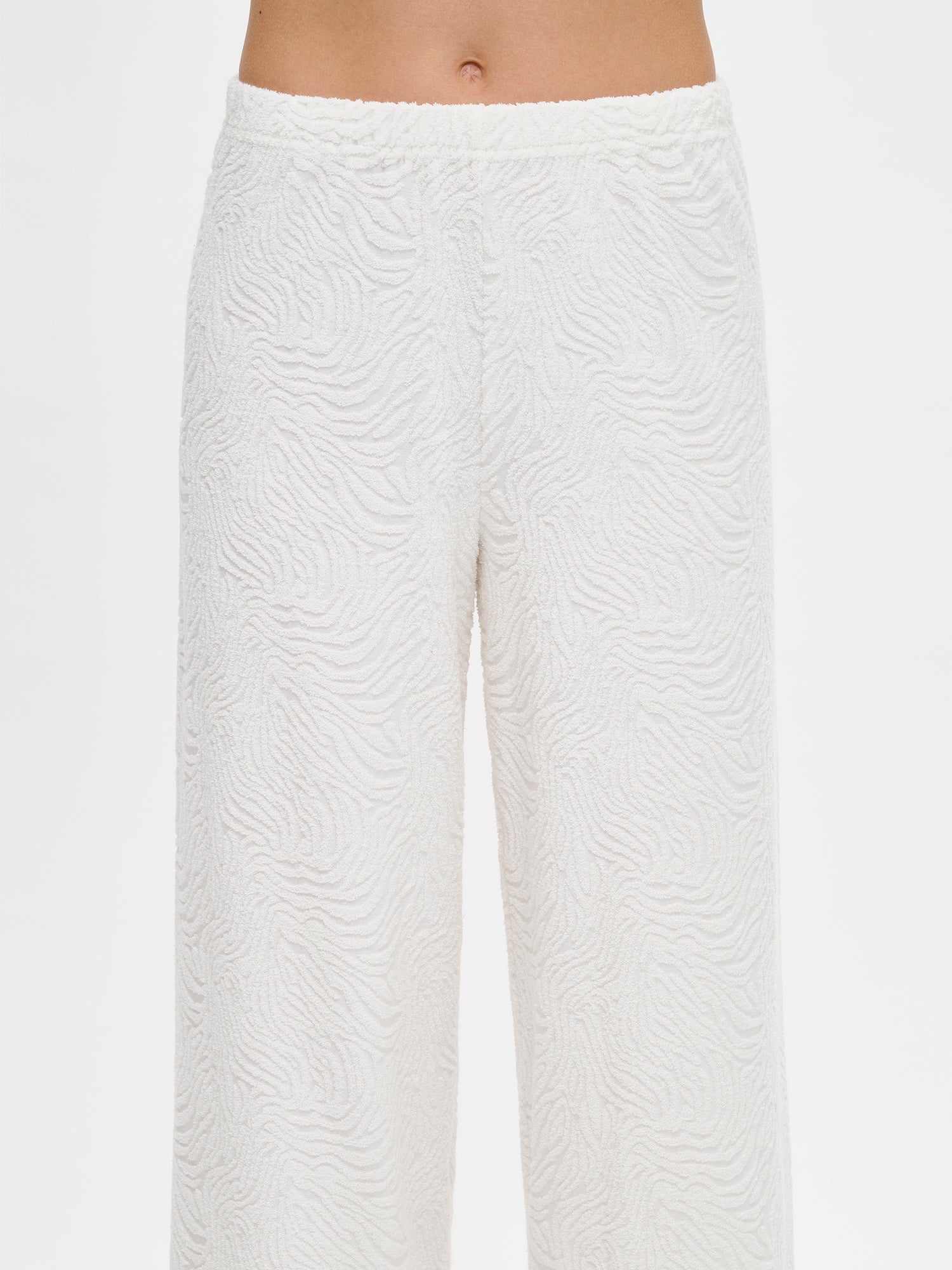 Nanso Väre relaxed-fit lounge pants with a beautifully textured fabric offer full-length coverage with an elastic waistband that provides a comfortable, secure fit throughout the day. On a model, close-up.