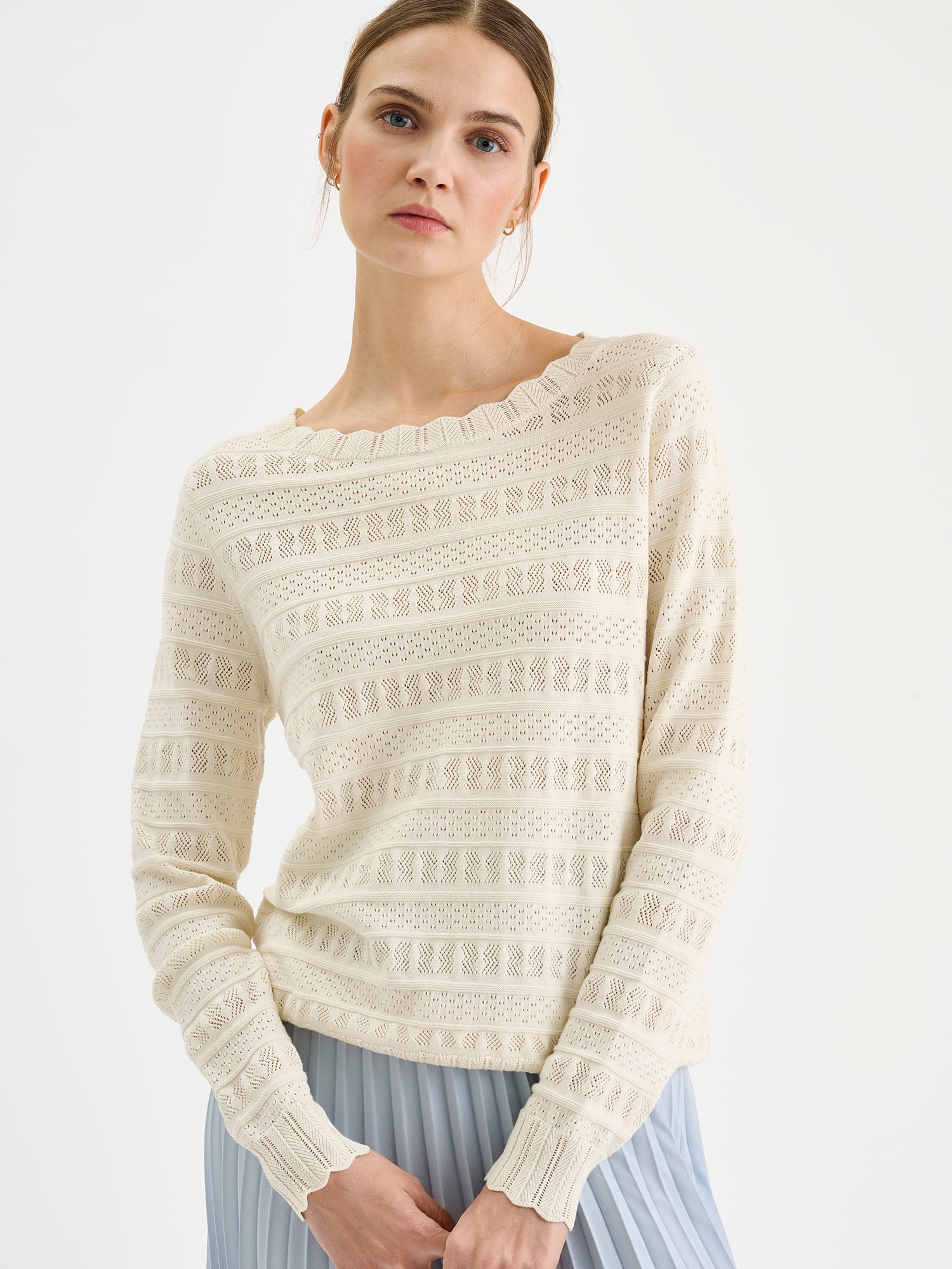 Nanso timeless white KORU knit sweater featuring delicate lace knit on a model with a pleated skirt, close-up