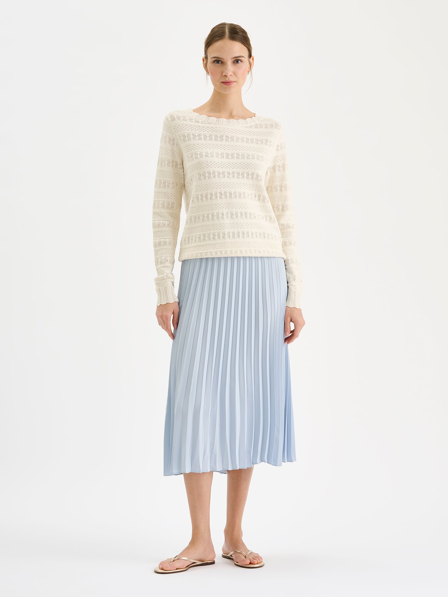 Nanso timeless white KORU knit sweater featuring delicate lace knit on a model with a pleated skirt