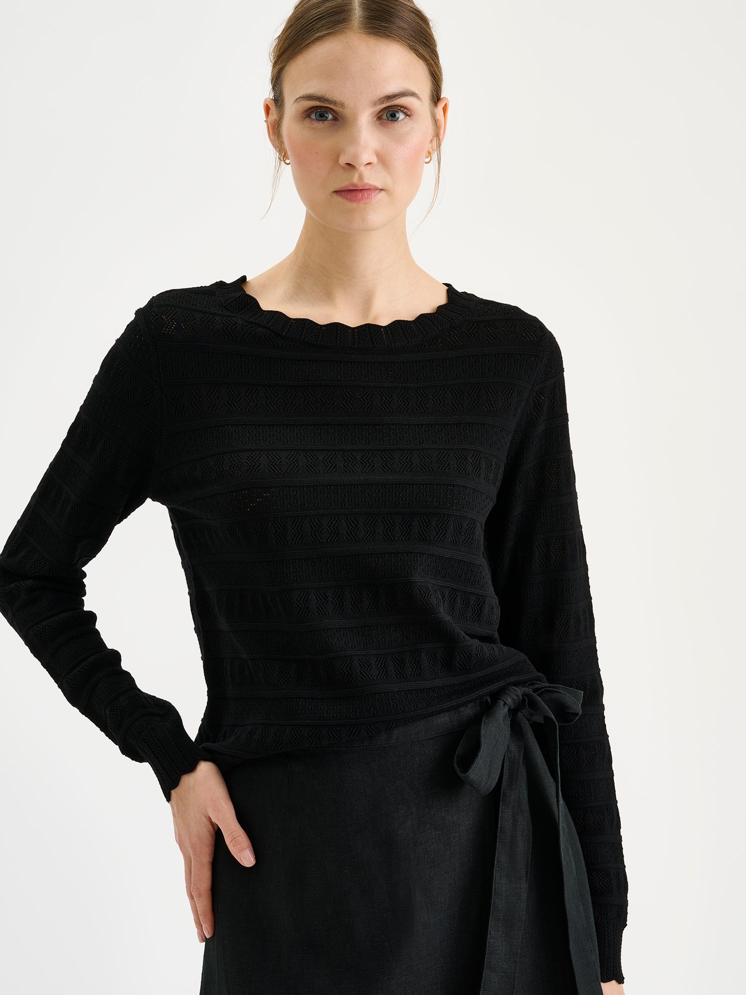 Nanso timeless black KORU knit sweater featuring delicate lace knit on a model with a linen skirt, close-up.
