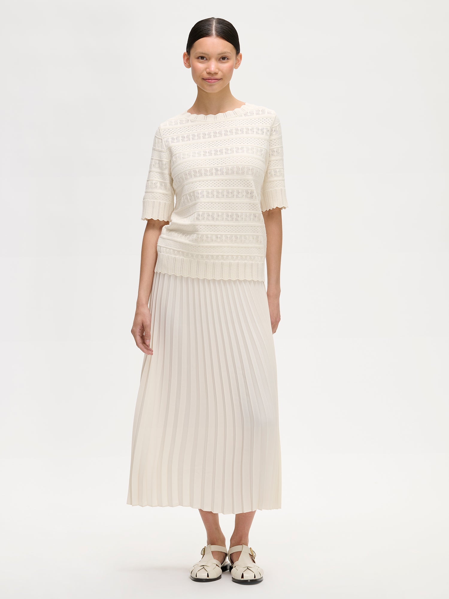 ARIEL pleated midi-length skirt in a fresh white shade on a model with a lace knit sweater.