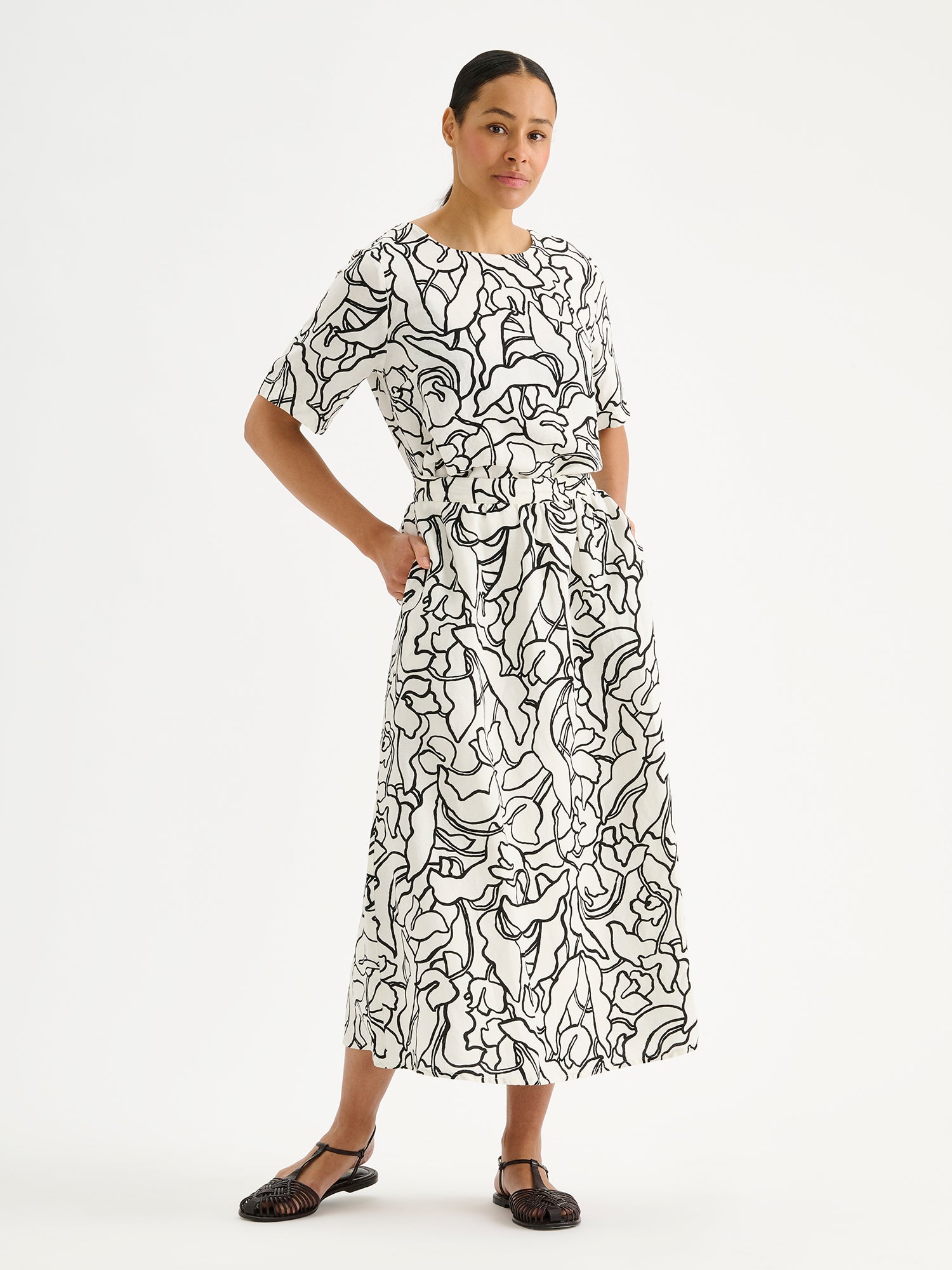 Nanso women's stylish and wonderfully relaxed IIRIS blouse featuring half-length sleeves and an elegant black and white floral pattern on a model with a matching skirt
