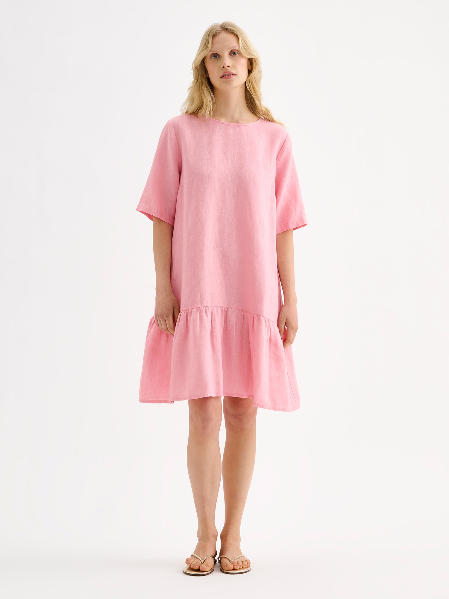 Nanso women's relaxed Liisu linen dress with half-length sleeves features a generously ruffled hem, on a model with sandals on.