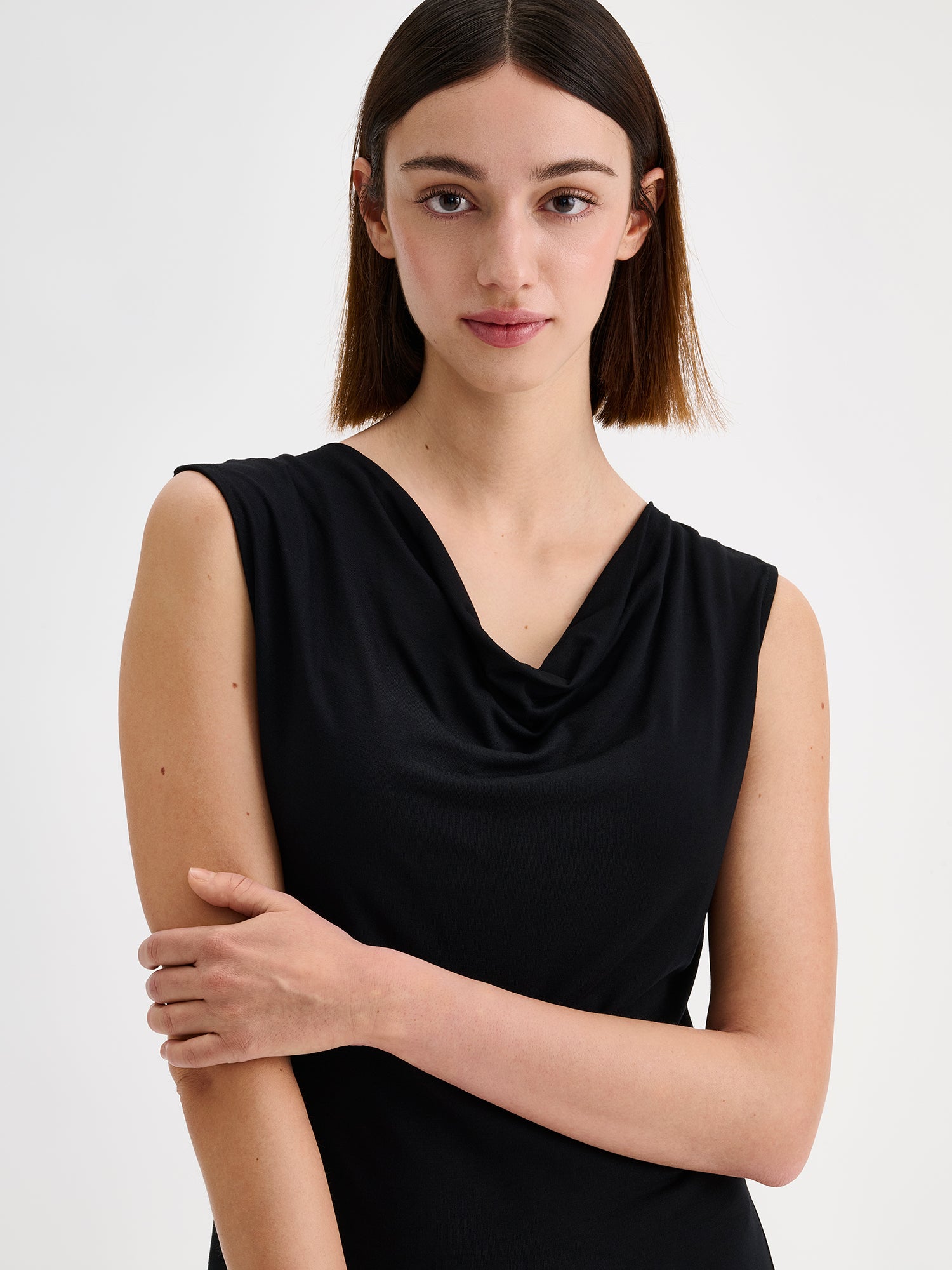 Nanso women's timeless Vivian black dress combines effortless style and comfort. This sleeveless maxi dress features an elegant draped neckline and a subtle side slit. Pictured on a brunette model, close-up.