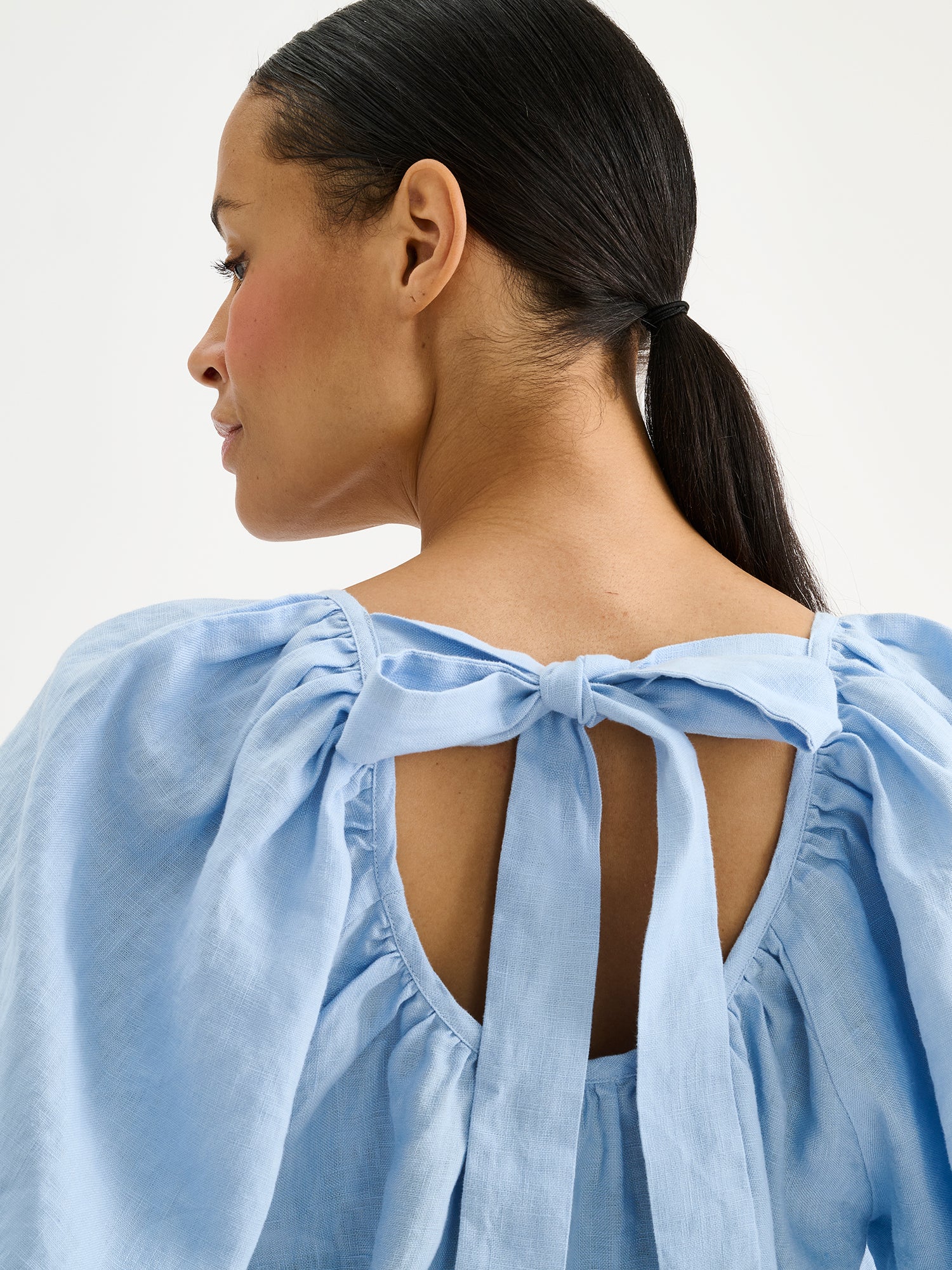 Nanso women's Donna linen blouse in a light blue shade on a model, close-up with a bow detail showing.