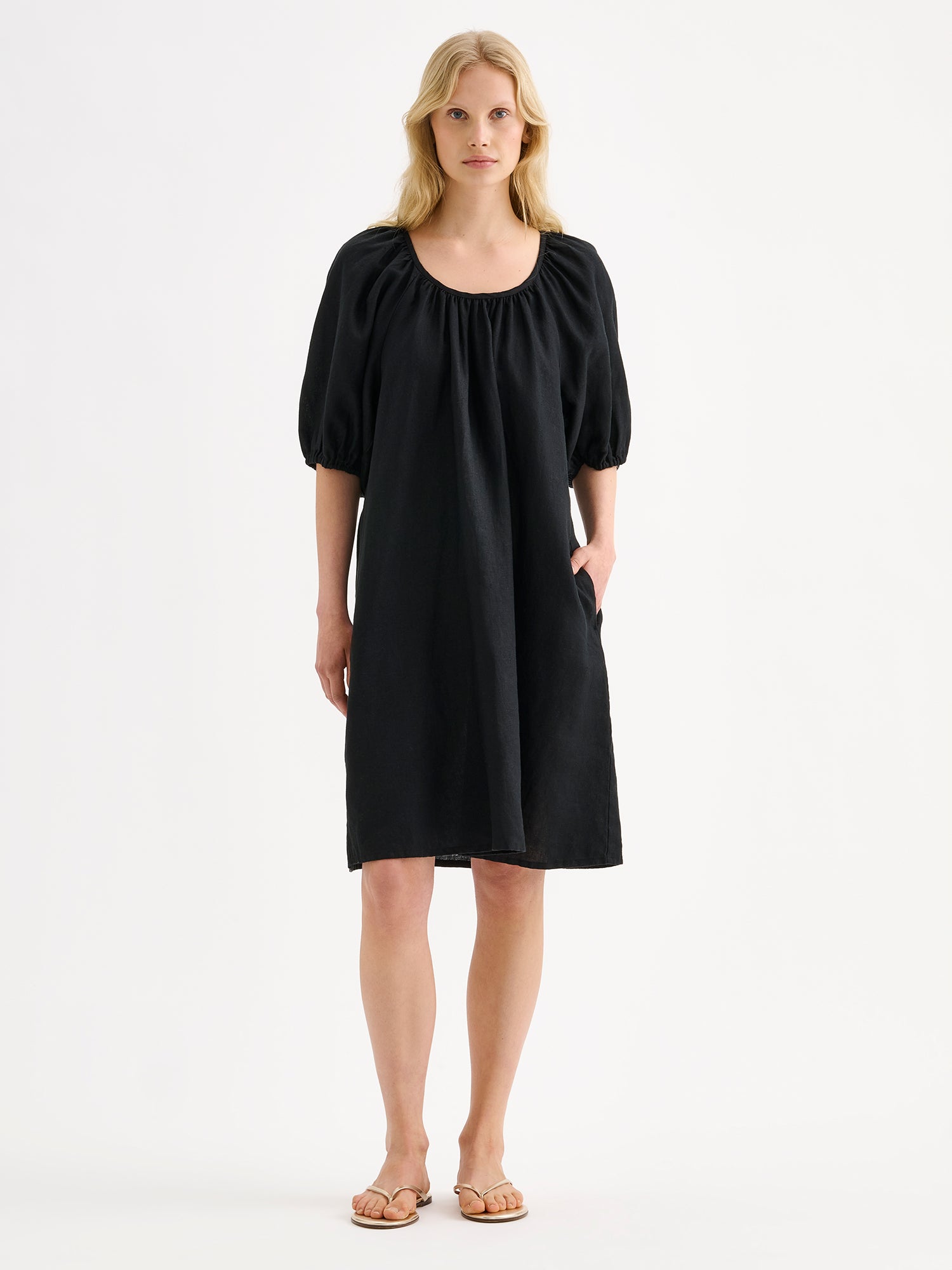 Nanso women’s beautifully relaxed black Donna linen dress. This airy short dress features a softly gathered open back neckline, finished with a tie-back bow detail. Pictured on a model.