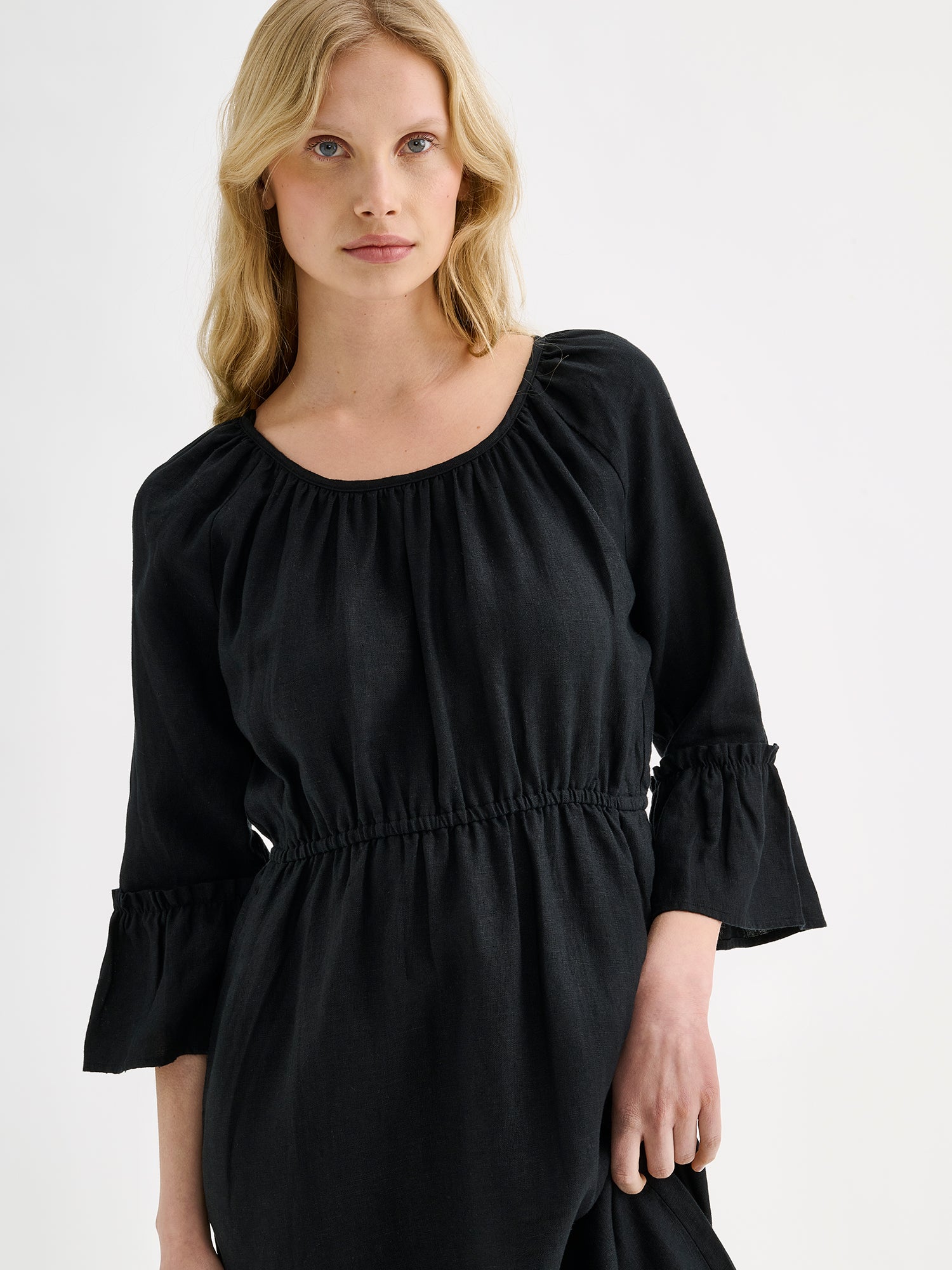 Nanso women's black  Donna midi linen dress combines effortless elegance with feminine details. This airy midi-length style features an open, softly gathered back neckline with a striking self-tie bow. Pictured on a blonde model, close-up.