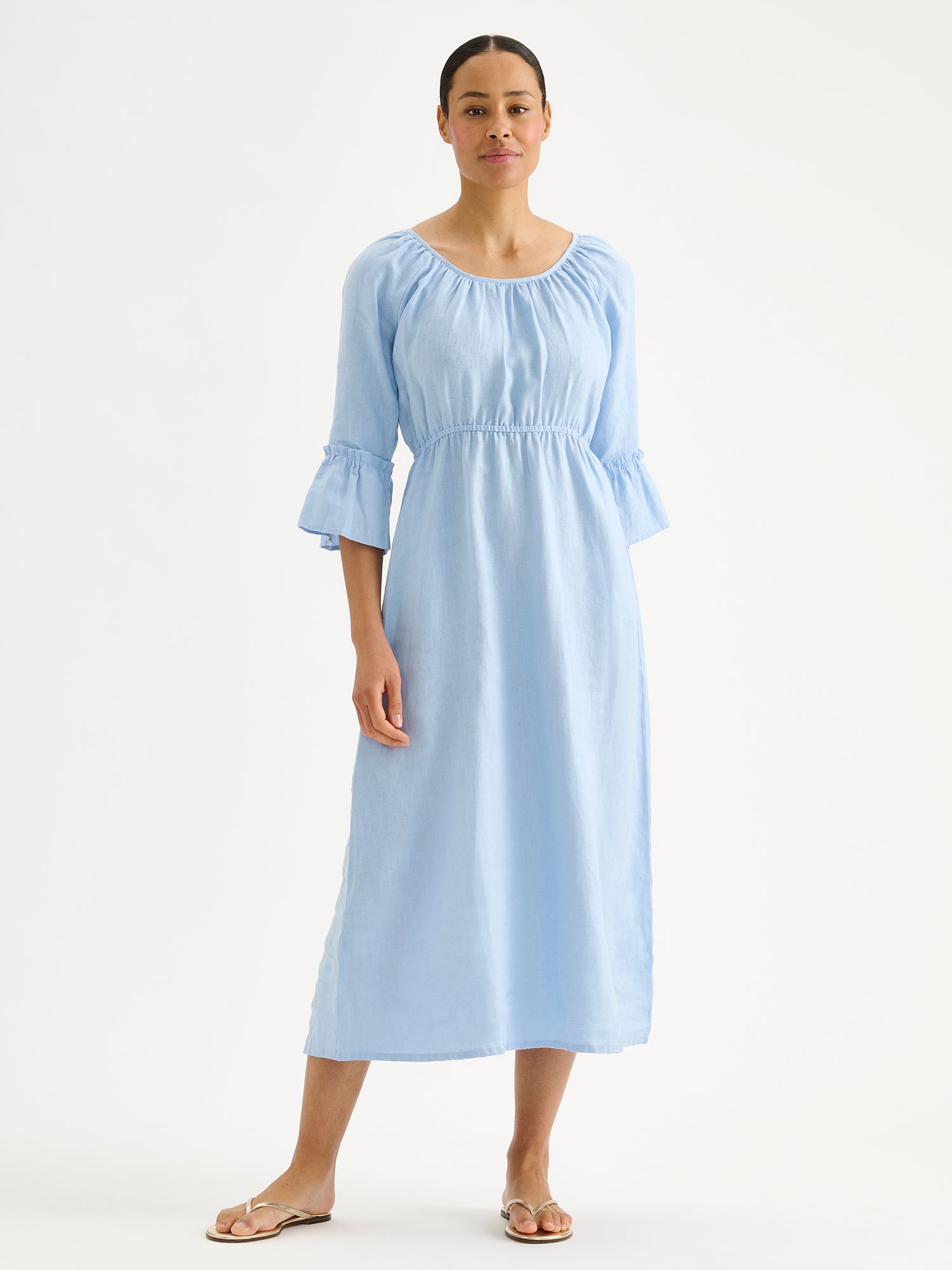 Nanso women's softly light blue Donna midi linen dress combines effortless elegance with feminine details. This airy midi-length style features an open, softly gathered back neckline with a striking self-tie bow. Pictured on a brunette model with golden sandals.
