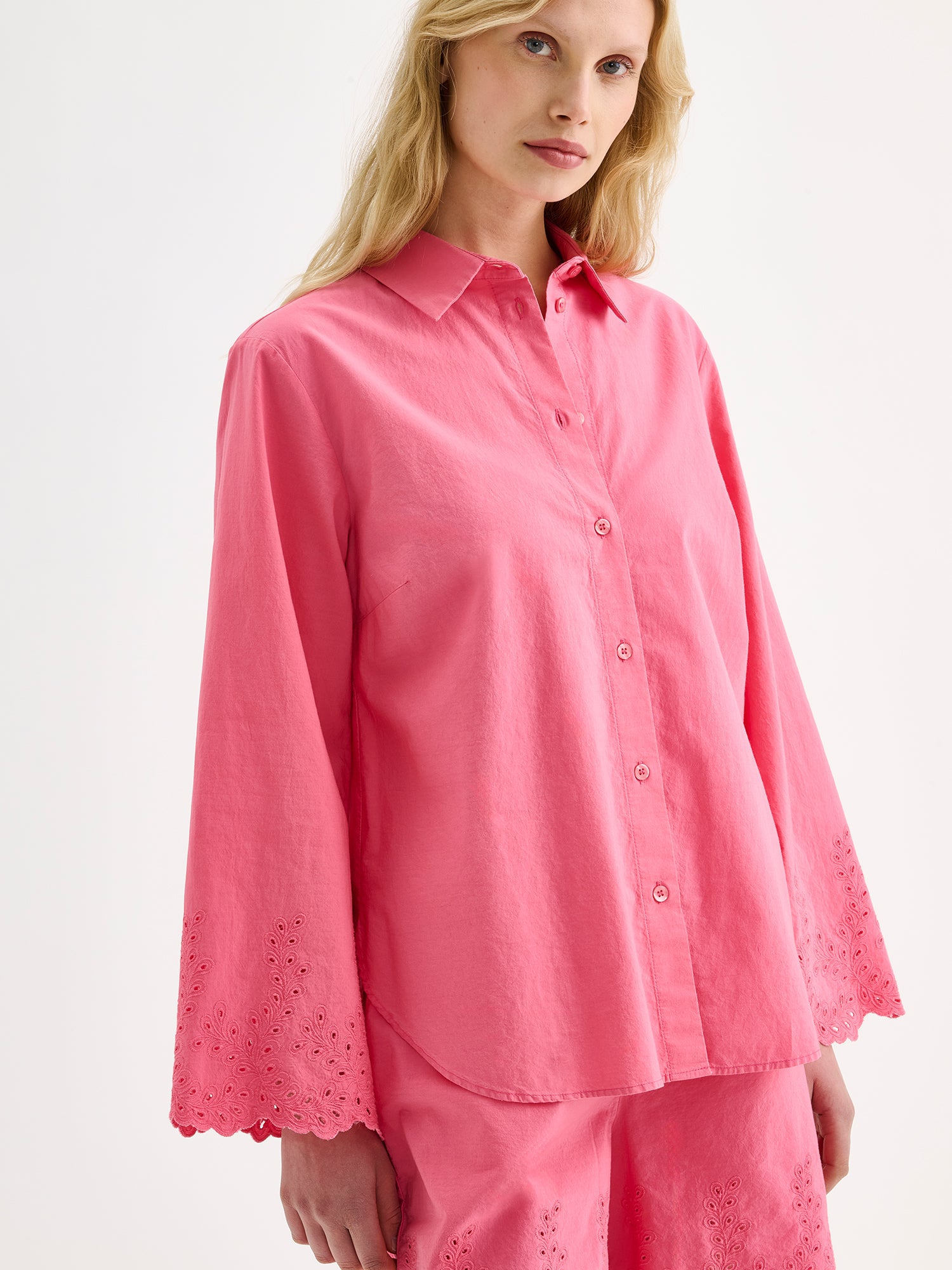 Nanso women's radiant pink Sevilla shirt with airy, relaxed sleeves and delicate lace-trimmed edges on a model with matching shorts, close-up.