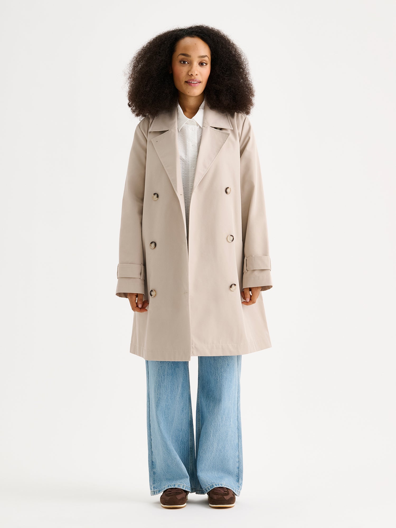 Nanso women's timeless midi trench coat in beige on a model with jeans, the coat open
