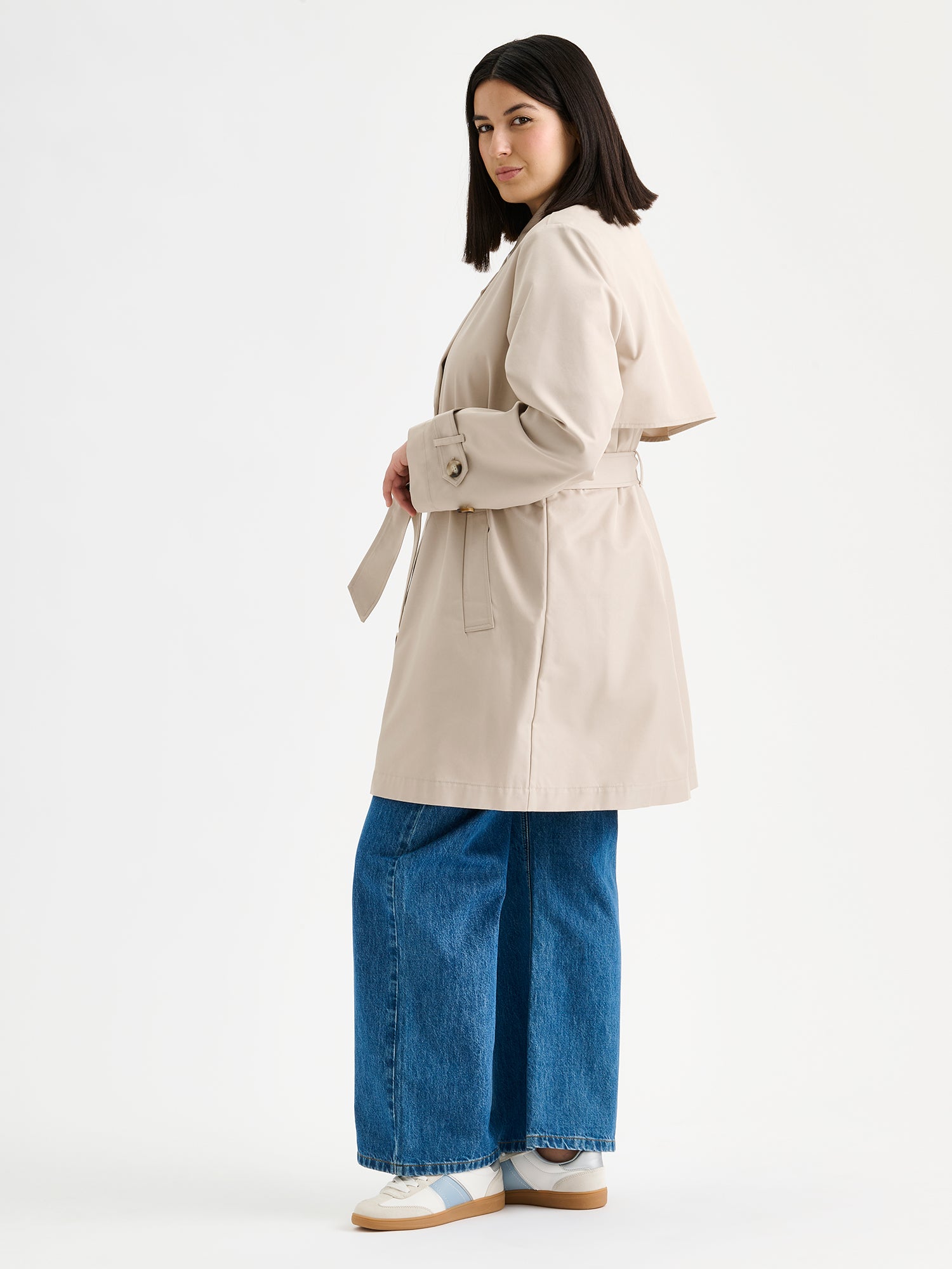 Nanso women's timeless midi trench coat in beige on a model with jeans pictured from the side.