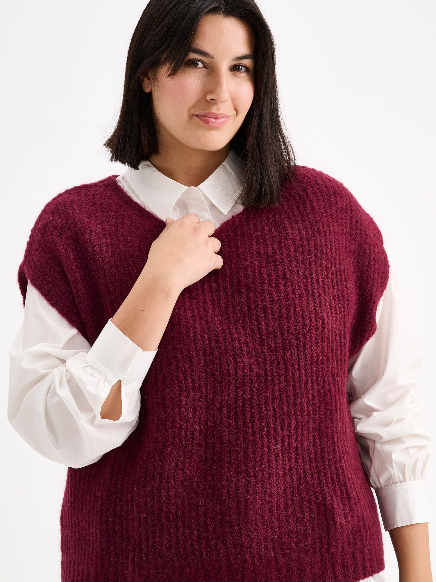 Nanso women's luxuriously soft and wonderfully chunky, the Karamelli knitted vest in a rich wine-red hue on a model with a white shirt