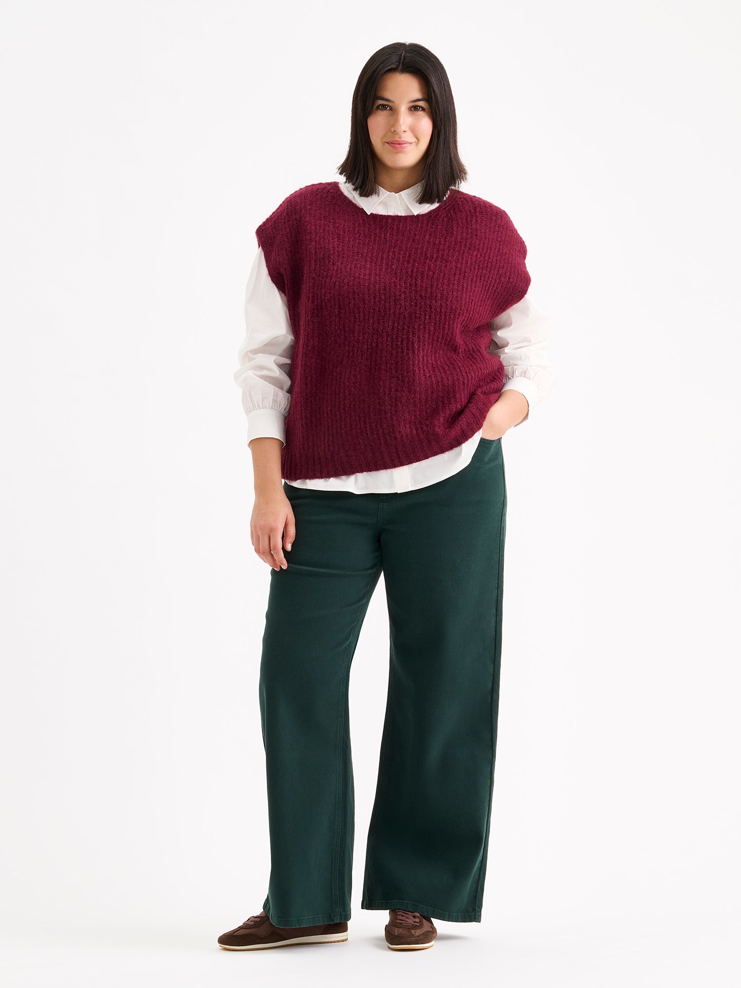 Nanso women's luxuriously soft and wonderfully chunky, the Karamelli knitted vest in a rich wine-red hue on a model with a white shirt and green jeans