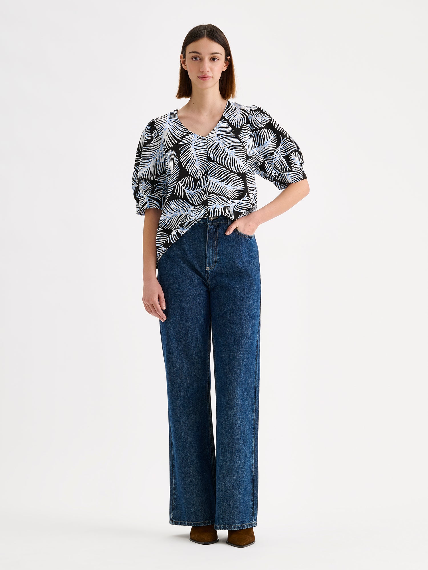Nanso women's patterned Hilde blouse captivates with its elegant graphic and delicate pattern, flattering V-neckline and puff-sleeves. Pictured on a model with wide blue jeans.