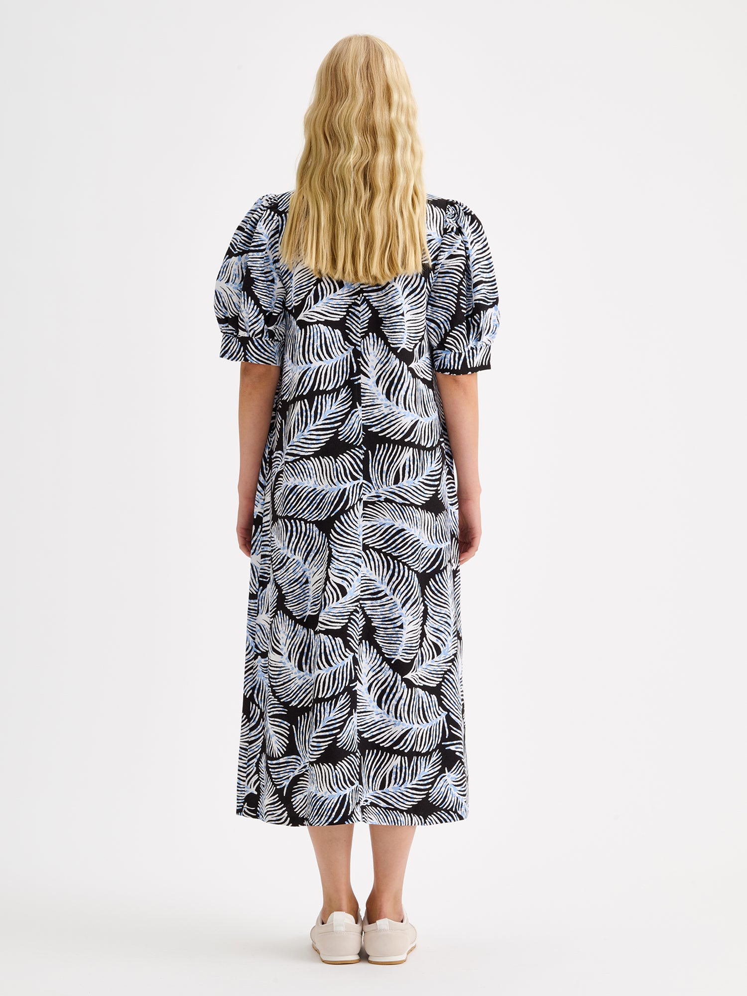 Nanso women's midi Hilde dress in a stylish and delicate black and blue-white print on a blonde model with sneakers, pictured from the backside