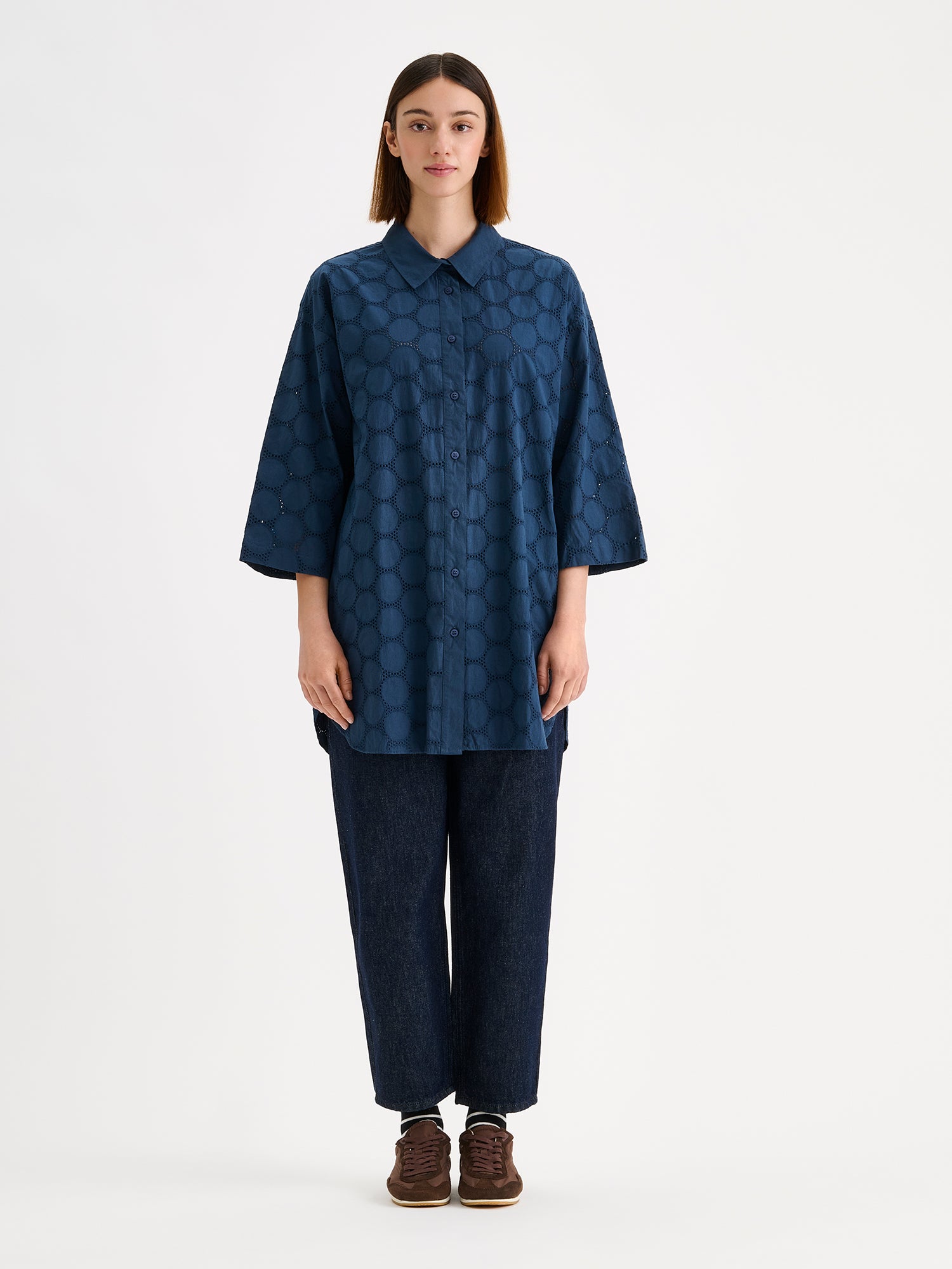Nanso women's SIIRI Long Shirt in blue is a relaxed-fit women's shirt with an elegant embroidered lace-like pattern, classic collar and buttons, on a model with jeans
