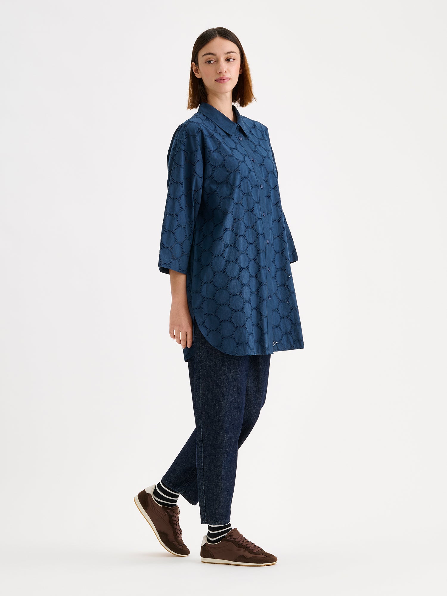 Nanso women's SIIRI Long Shirt in blue is a relaxed-fit women's shirt with an elegant embroidered lace-like pattern, classic collar and buttons, on a model with jeans