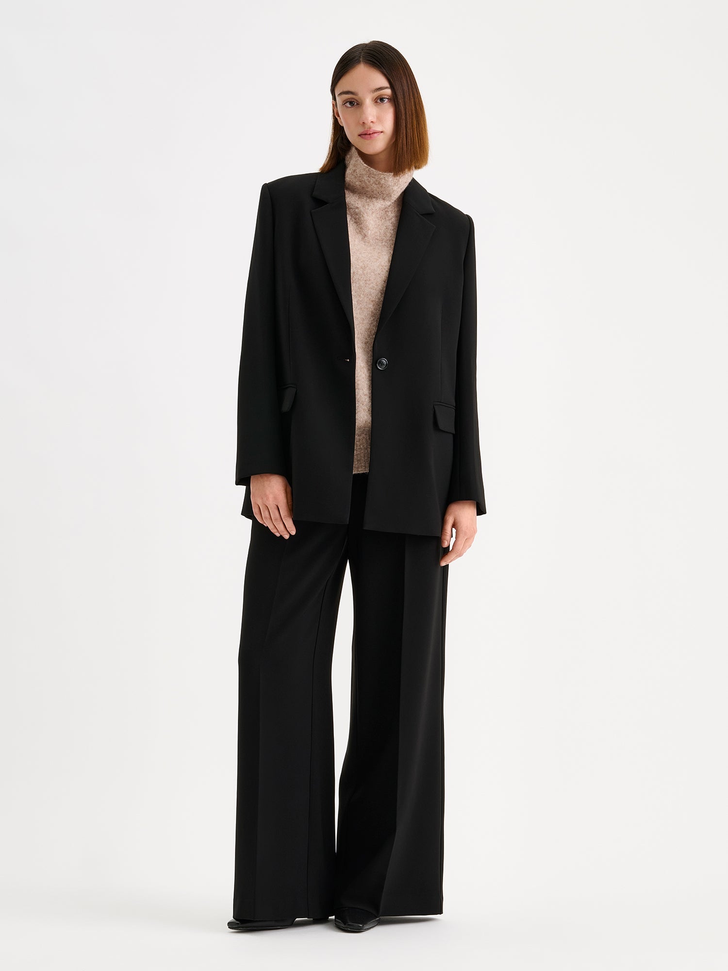 Nanso womens elegant and timeless wide-leg EEVA trousers in timeless black, on a model with a matching blazer and a beige knitted vest.