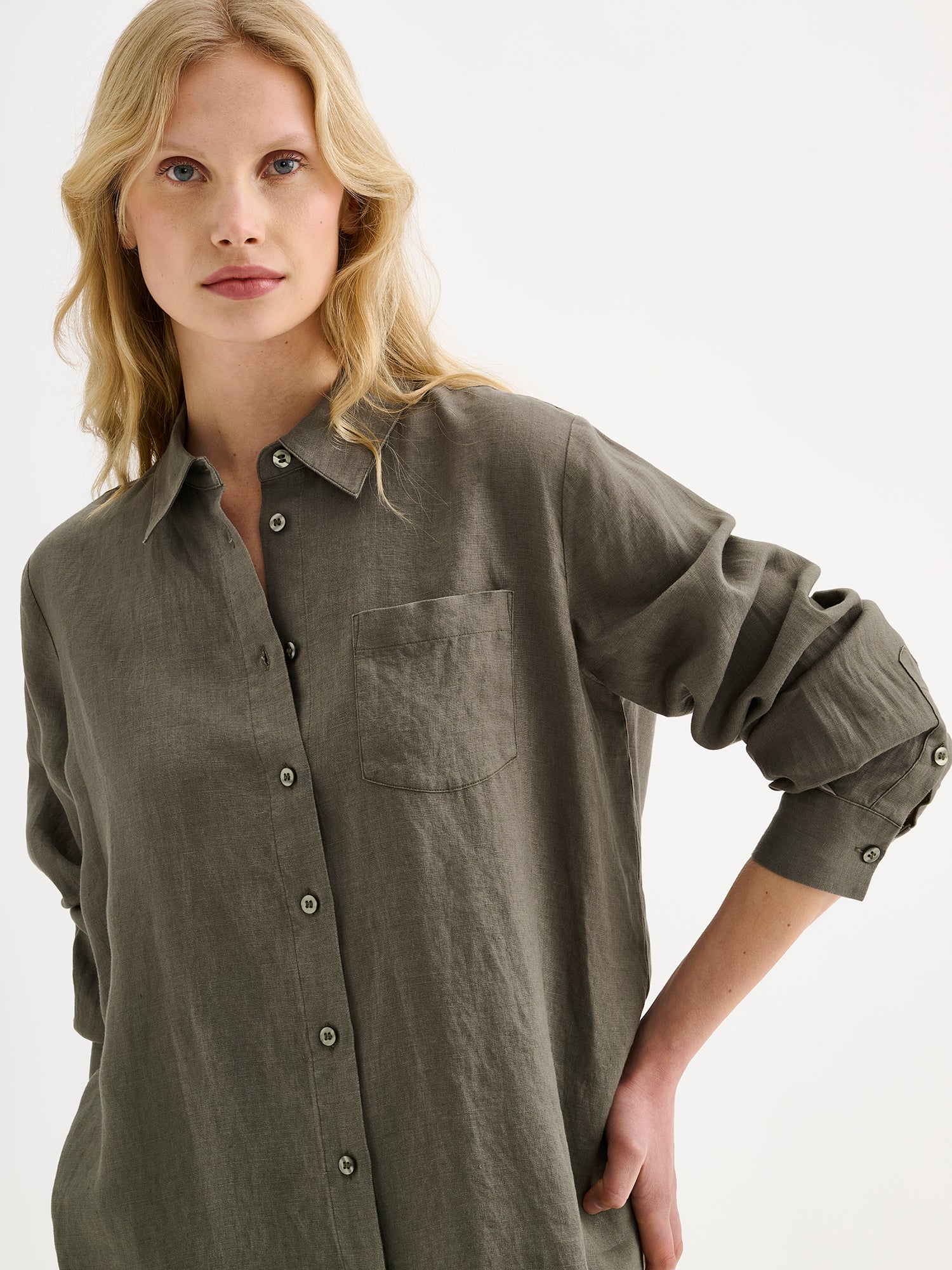 Nanso women's relaxed, classic and versatile olive green Lene linen shirt is crafted from woven linen fabric that is durable and breathable. The shirt features a front button closure and chest pocket and full-length sleeves. Pictured on a model, close-up.