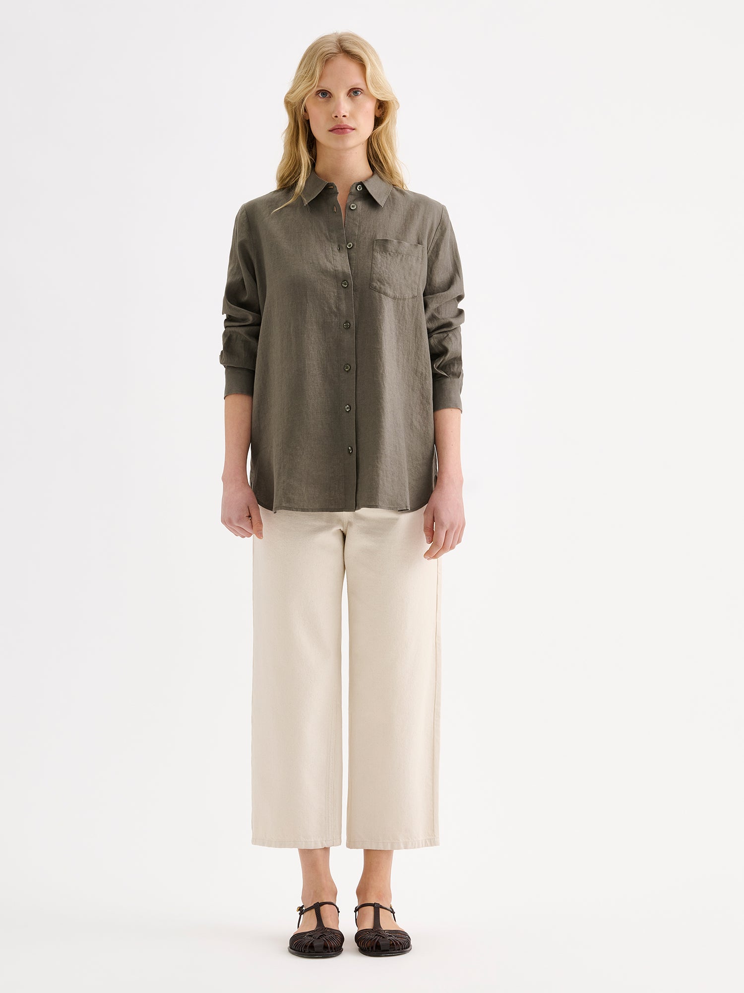 Nanso women's relaxed, classic and versatile olive green Lene linen shirt is crafted from woven linen fabric that is durable and breathable. The shirt features a front button closure and chest pocket and full-length sleeves. Pictured on a model 