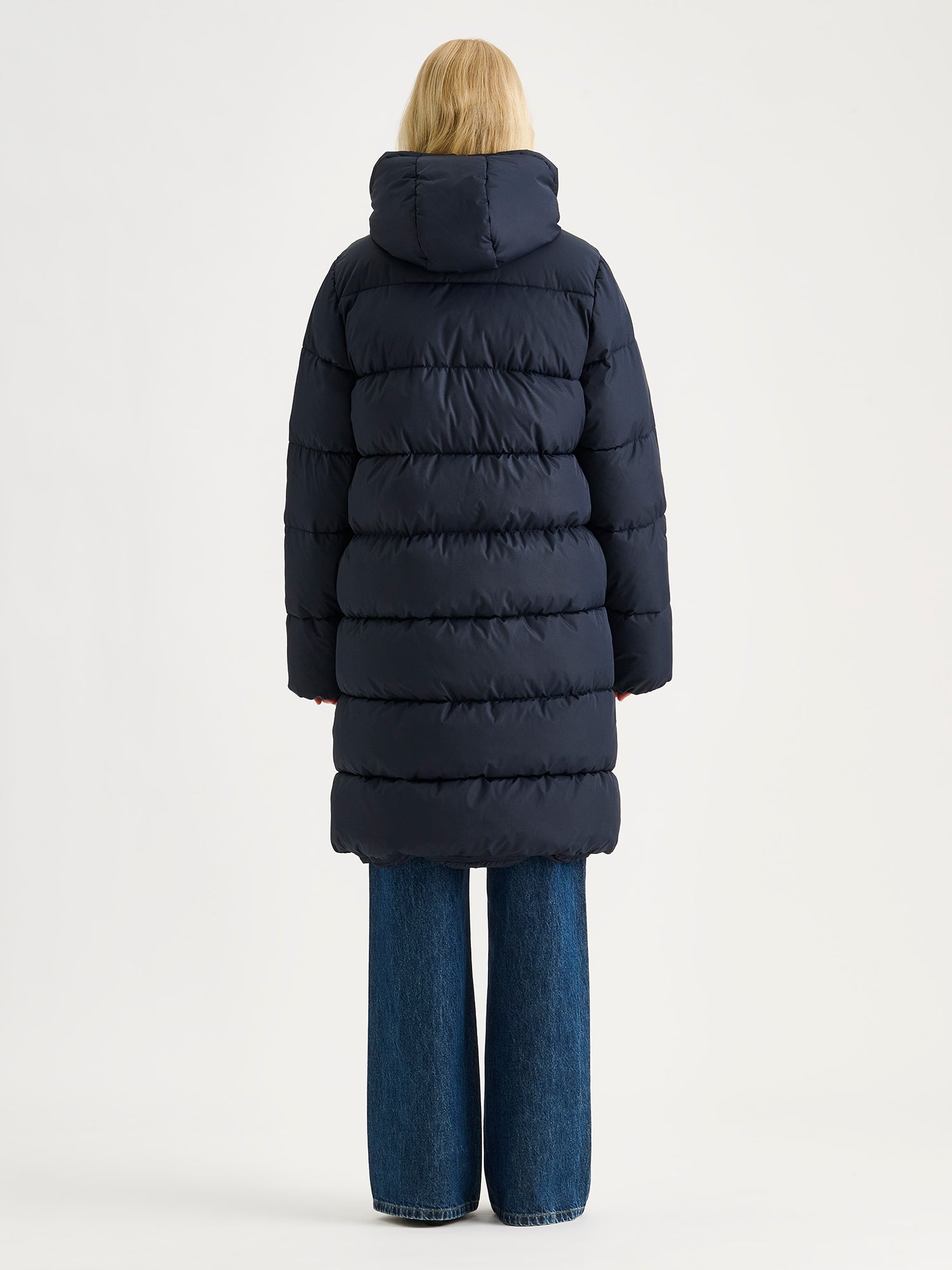 Nanso women's warm, padded yet pleasantly lightweight Lumi midi puffer coat in dark blue on a model, pictured from tue backside