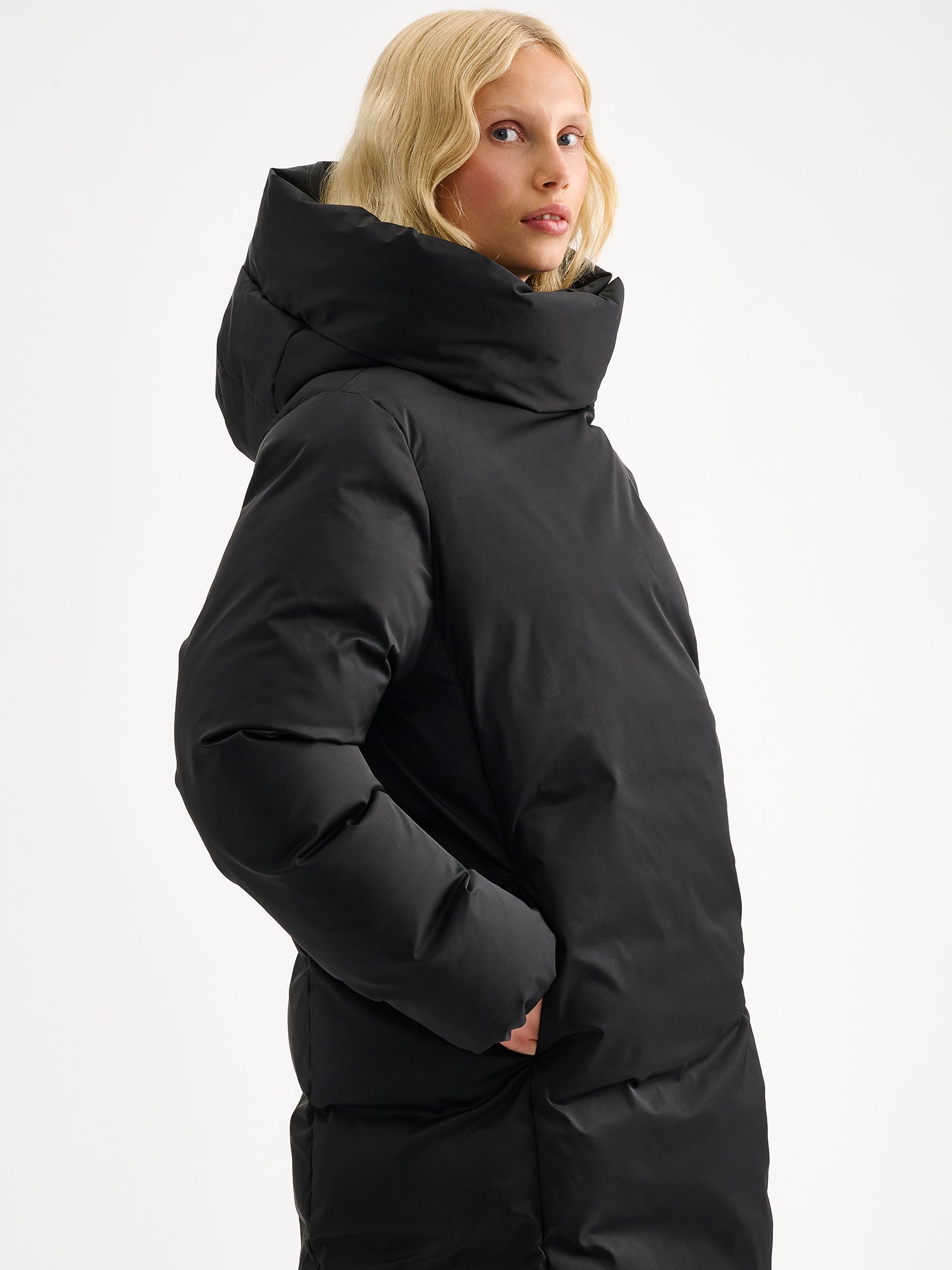 Warm and wonderfully voluminous, the long Inari puffer coat in black on a model, sideview.