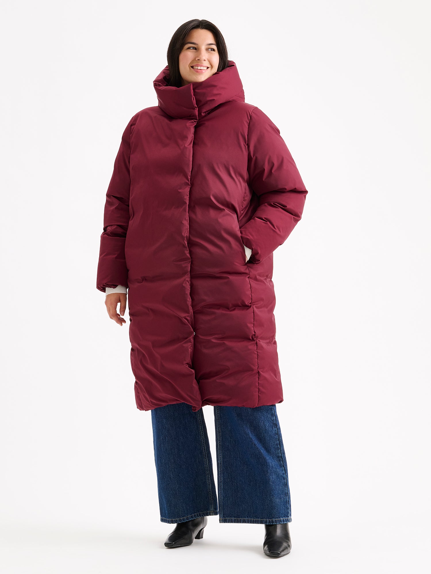 Warm and wonderfully voluminous, the long Inari puffer coat in winered on a model with jeans.