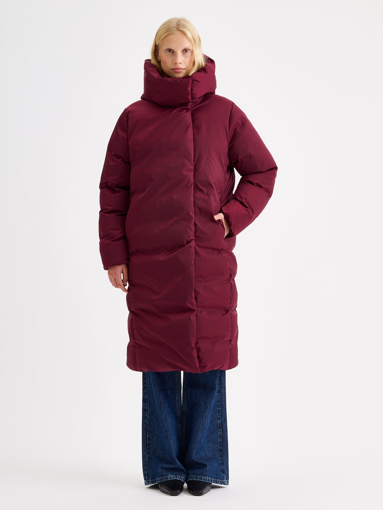 Warm and wonderfully voluminous, the long Inari puffer coat in winered on a model with jeans.