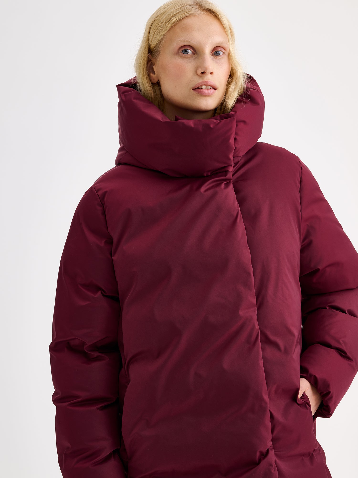 Warm and wonderfully voluminous, the long Inari puffer coat in winered on a model close-up.